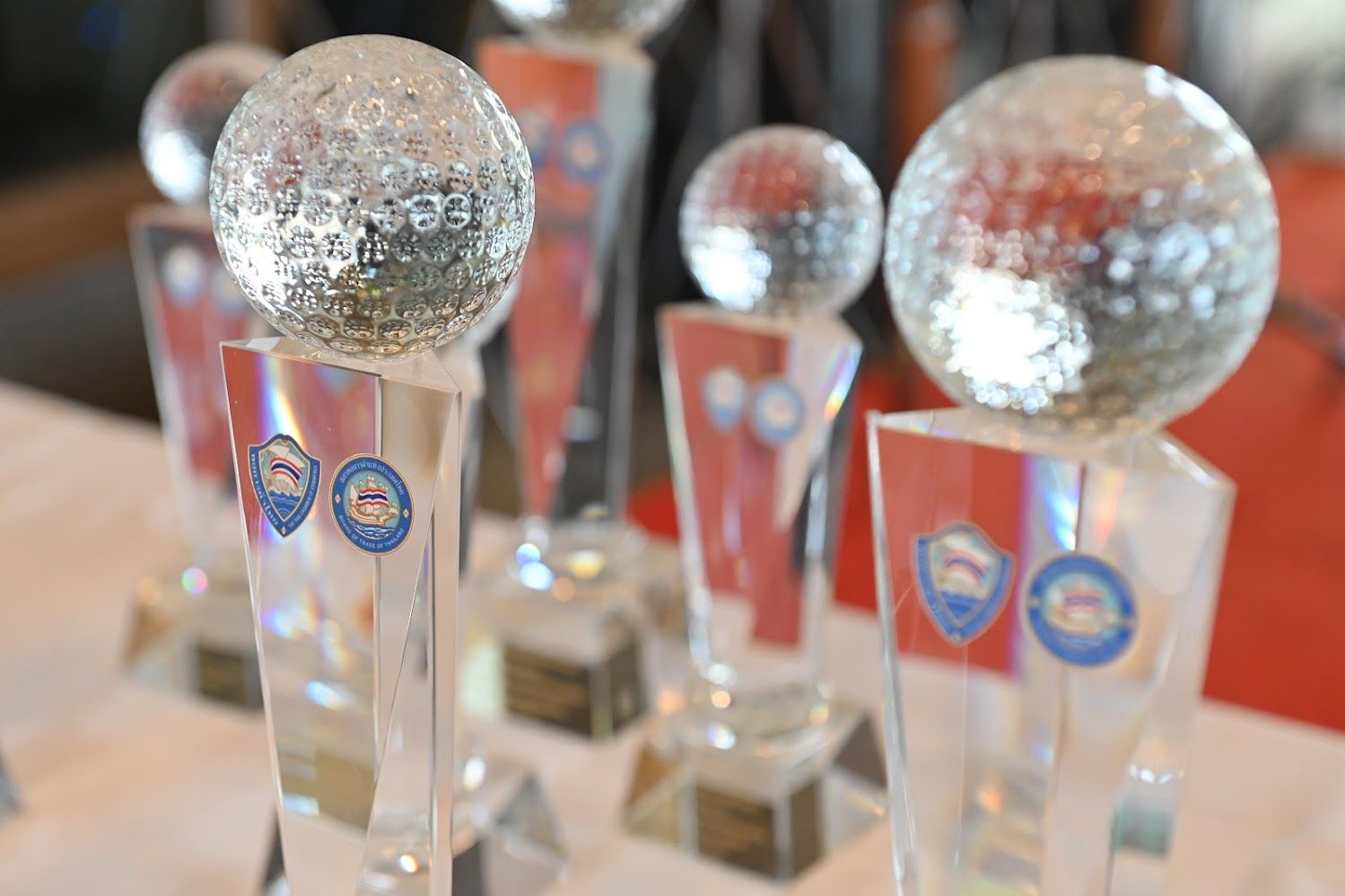 Clear, faceted golf ball trophies with red and white bases stand in a row.