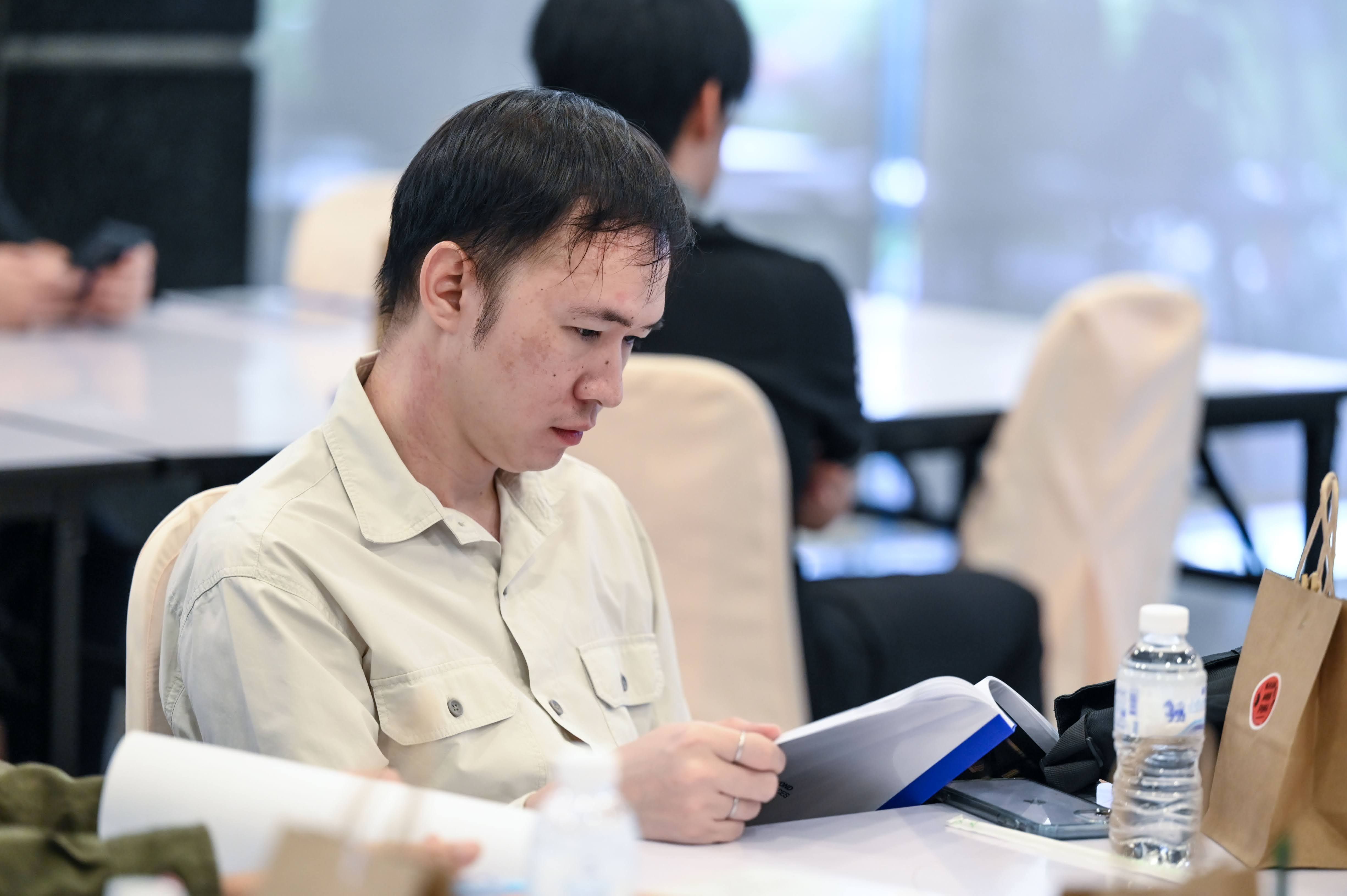 An Asian man in a beige shirt intently reads documents at a conference table.