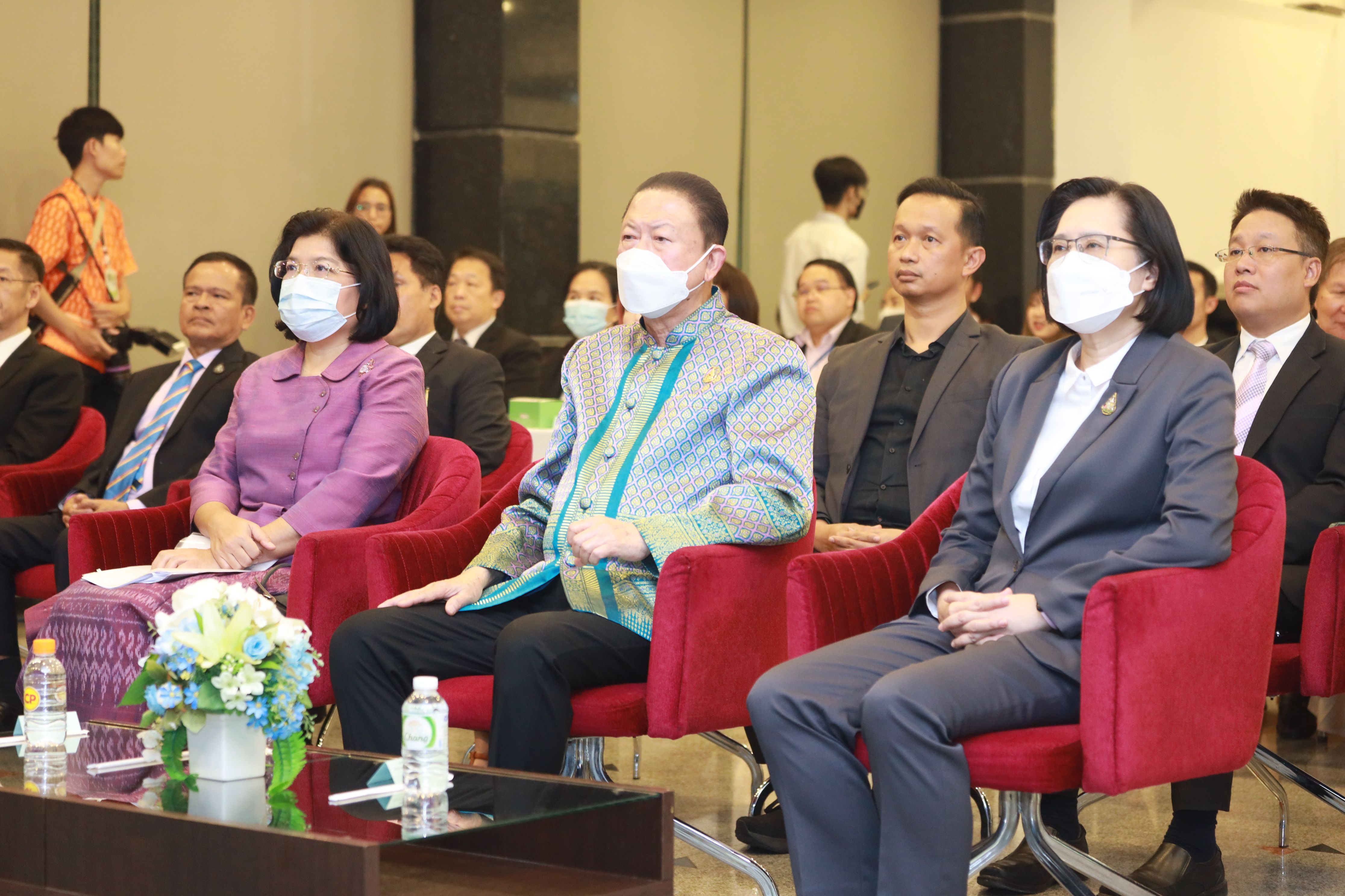 Officials wearing face masks attend a formal event, seated in an audience setting.
