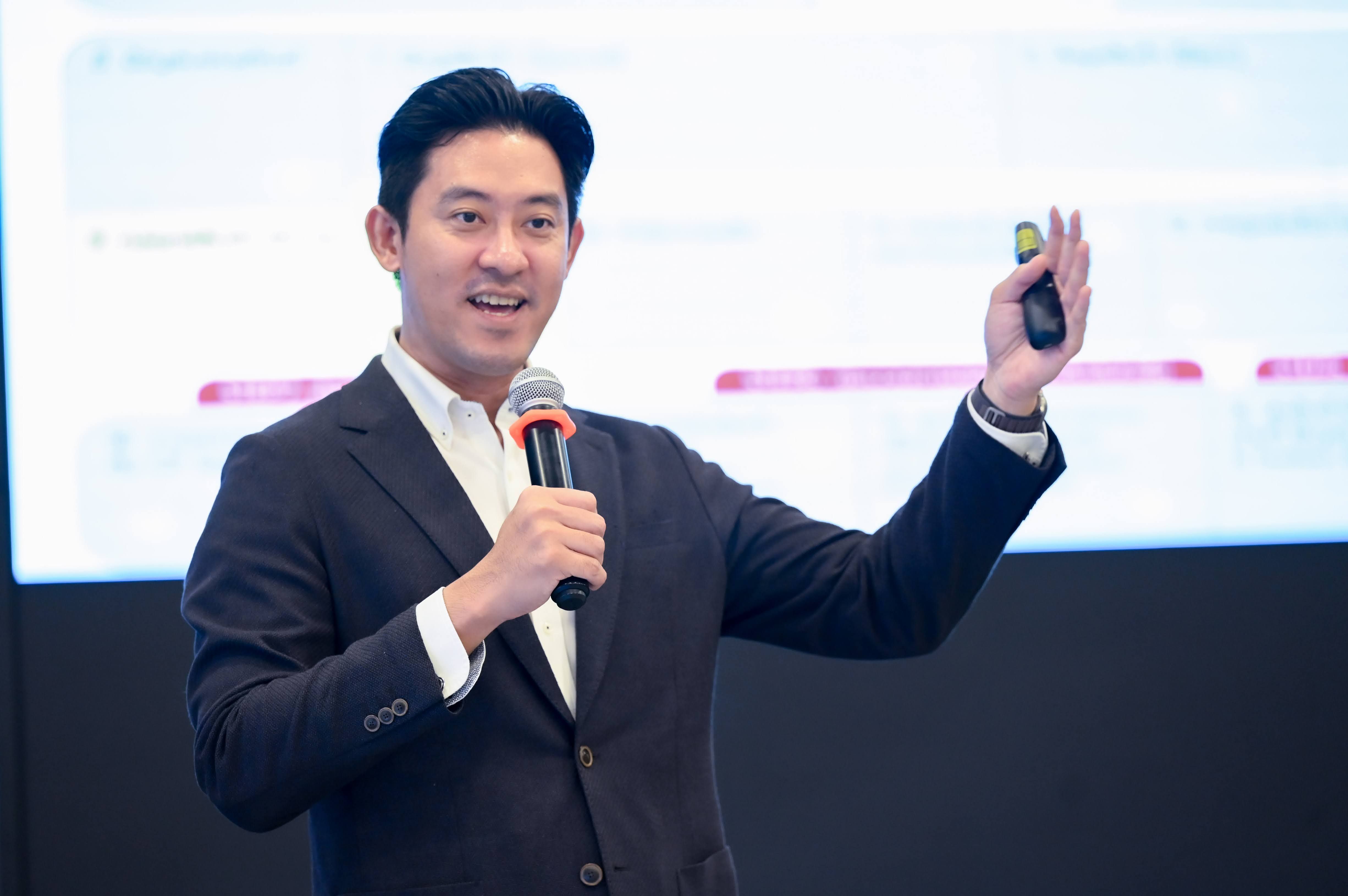 Professional speaker presenting with a microphone and remote control in front of a blurred screen.