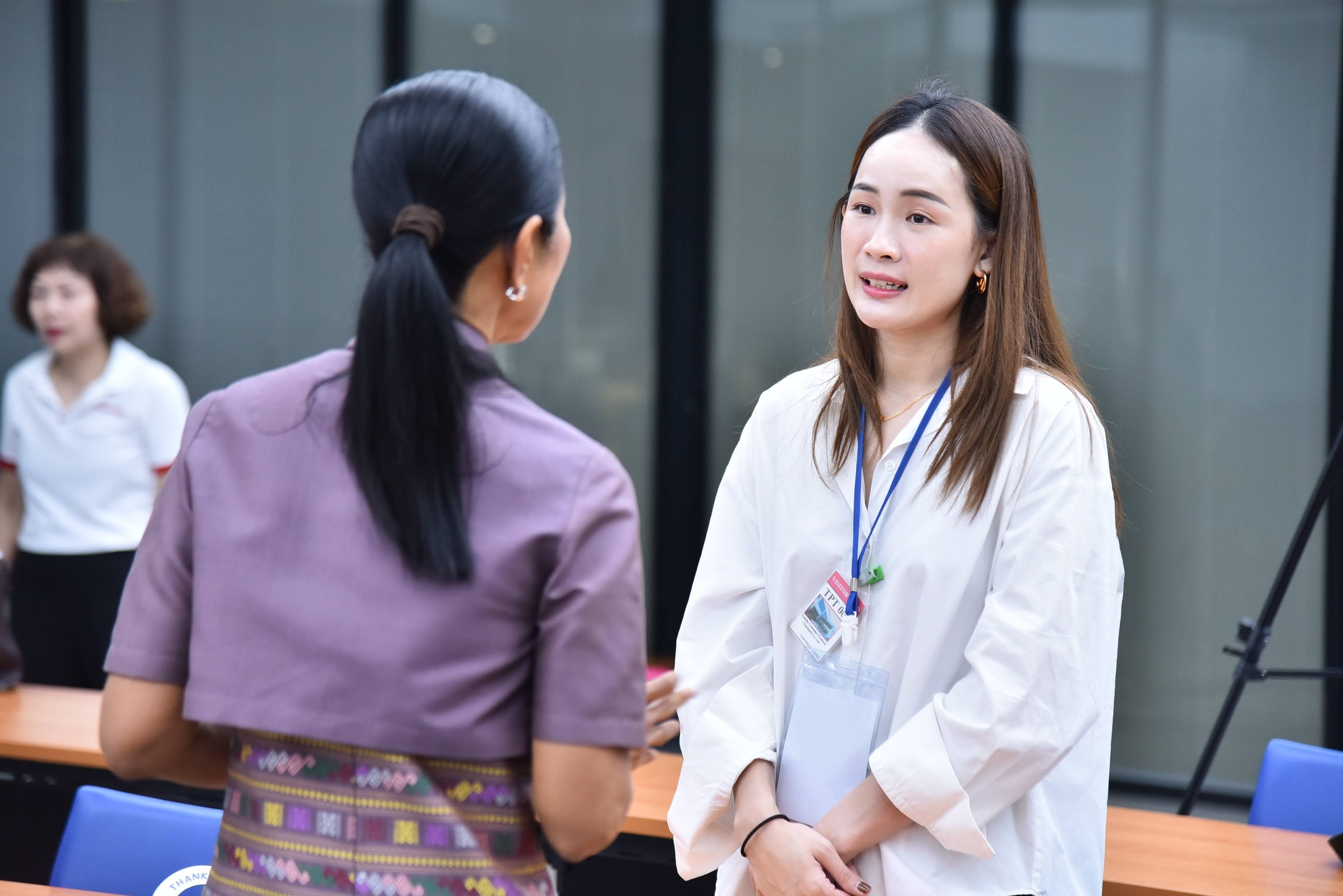 Two professional women engaging in a conversation inside an office or meeting room.