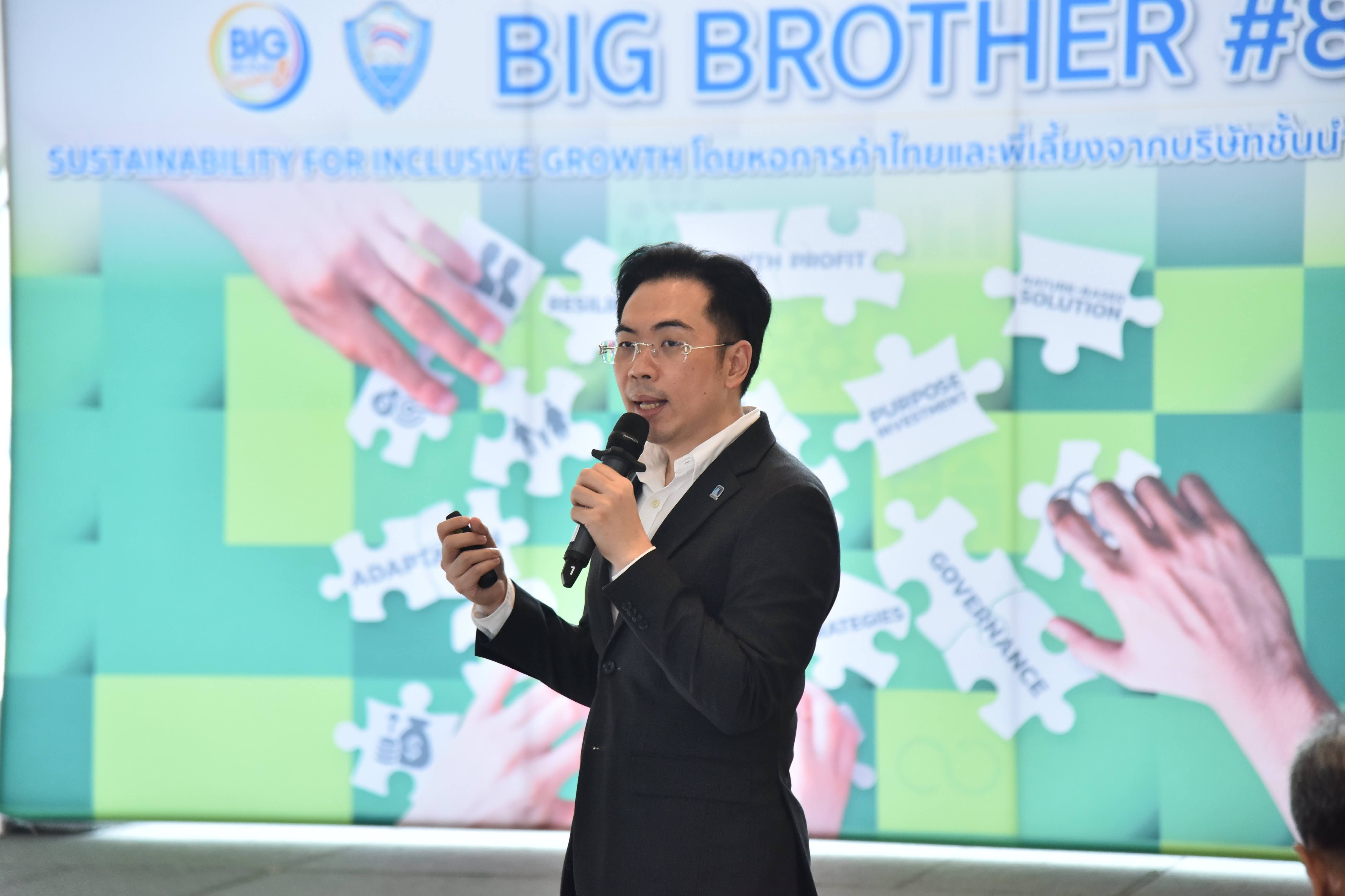 Man in a suit speaks into microphone before a screen displaying 'BIG BROTHER #8'.