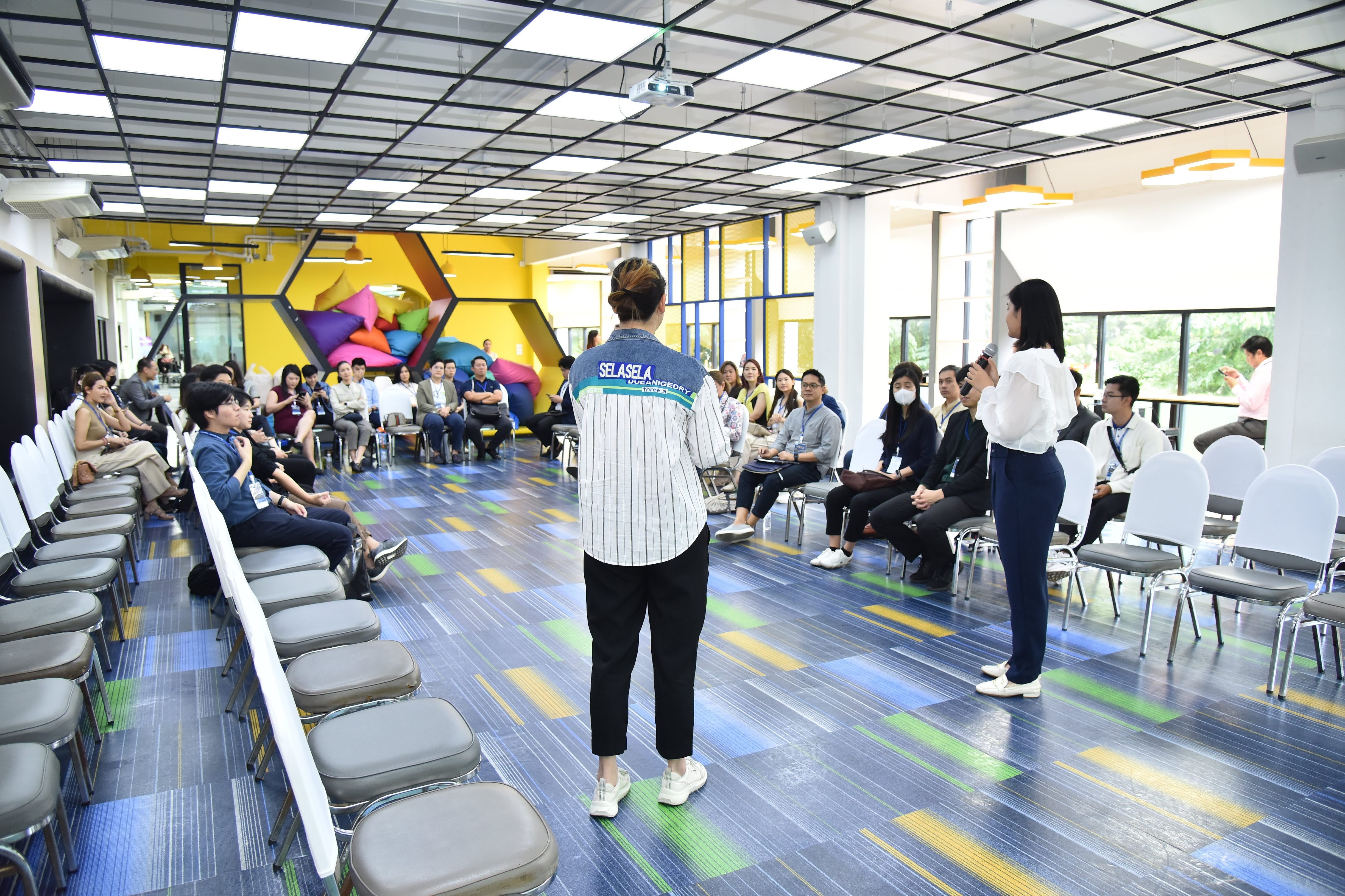 Two women lead a presentation to a seated audience in a modern, colorful room.