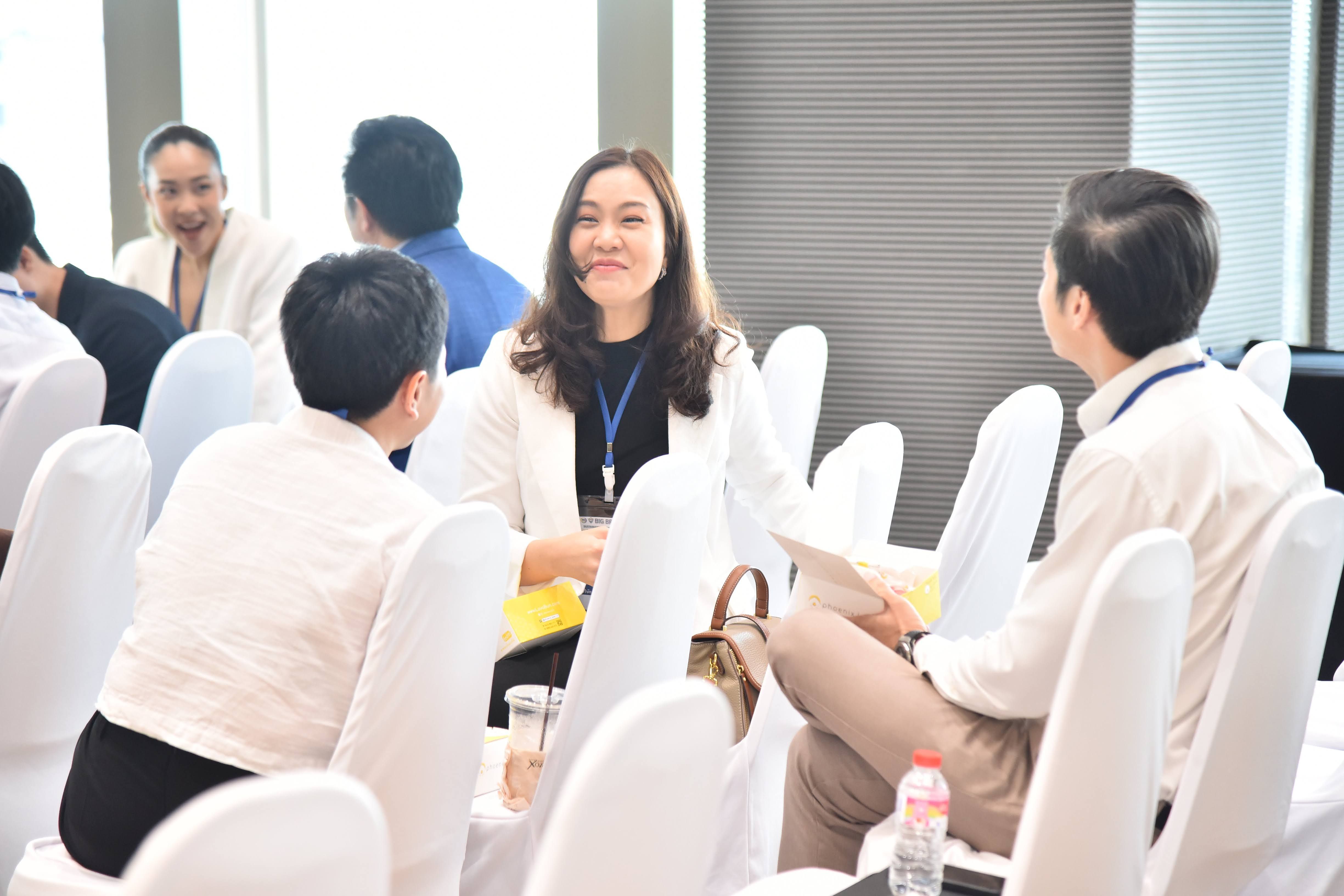 A smiling woman in a white blazer engages in conversation at a professional networking event.