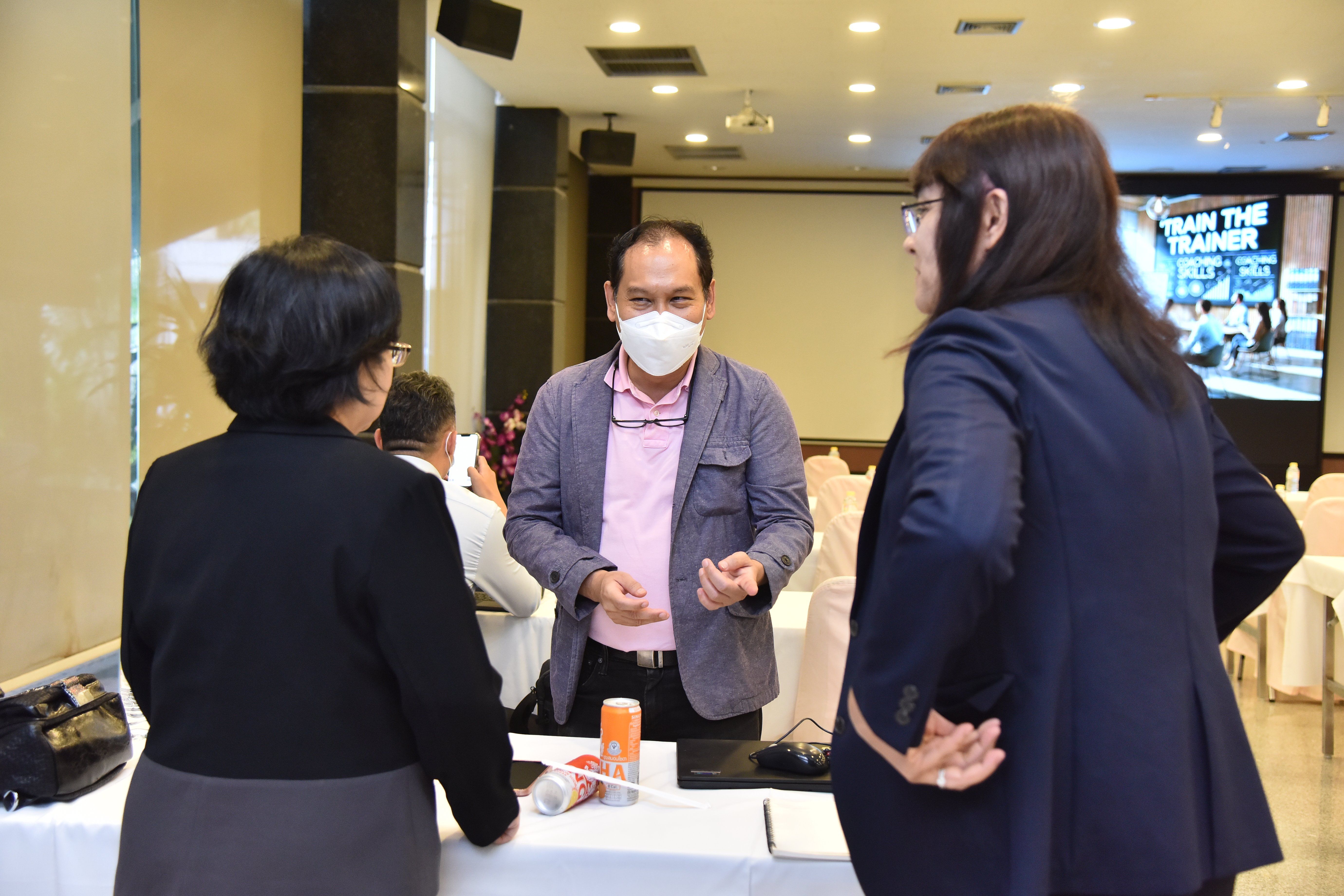 Three people discussing at a professional event, one man wears a face mask.