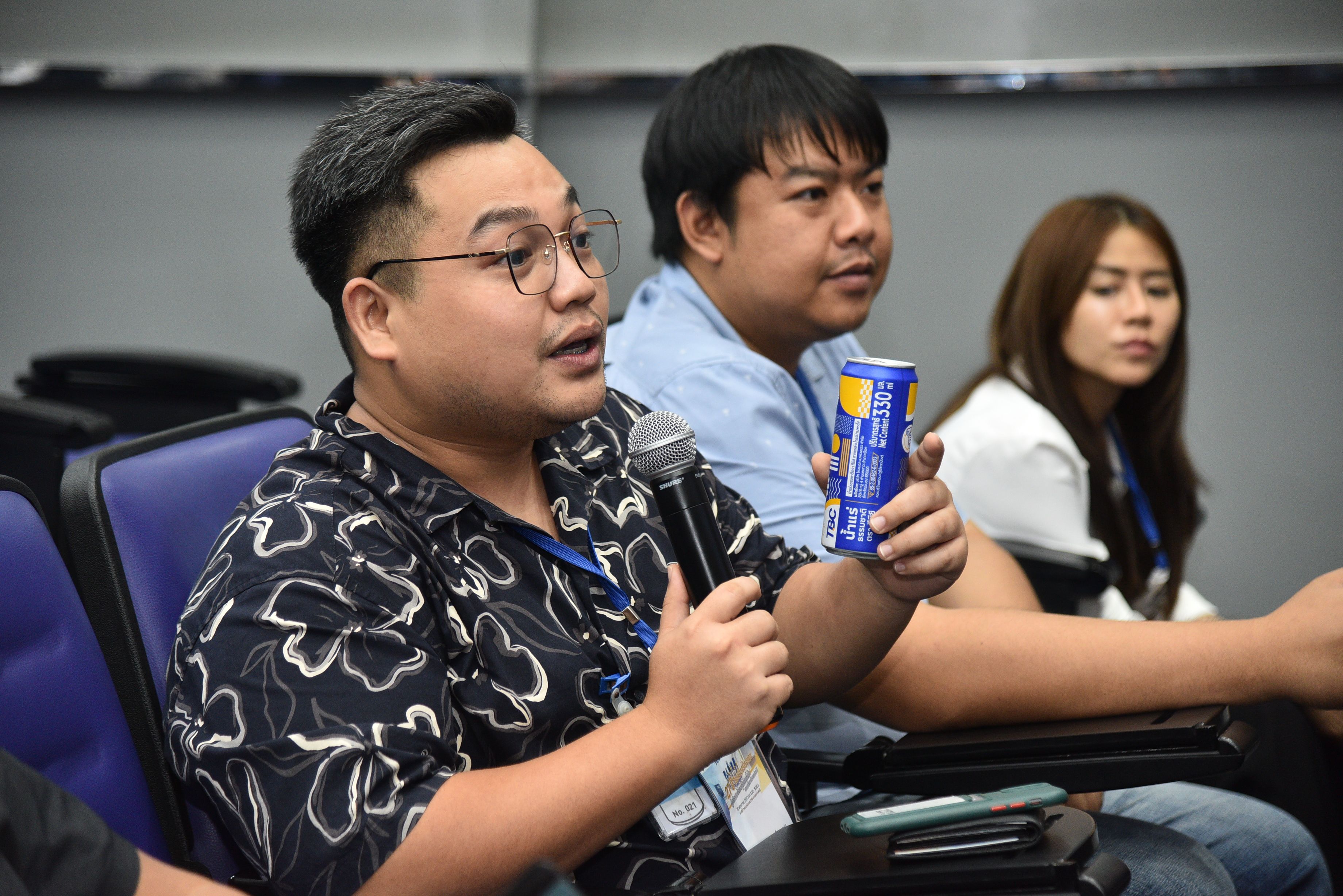 Man speaks into microphone, holding a blue and yellow can during a conference.