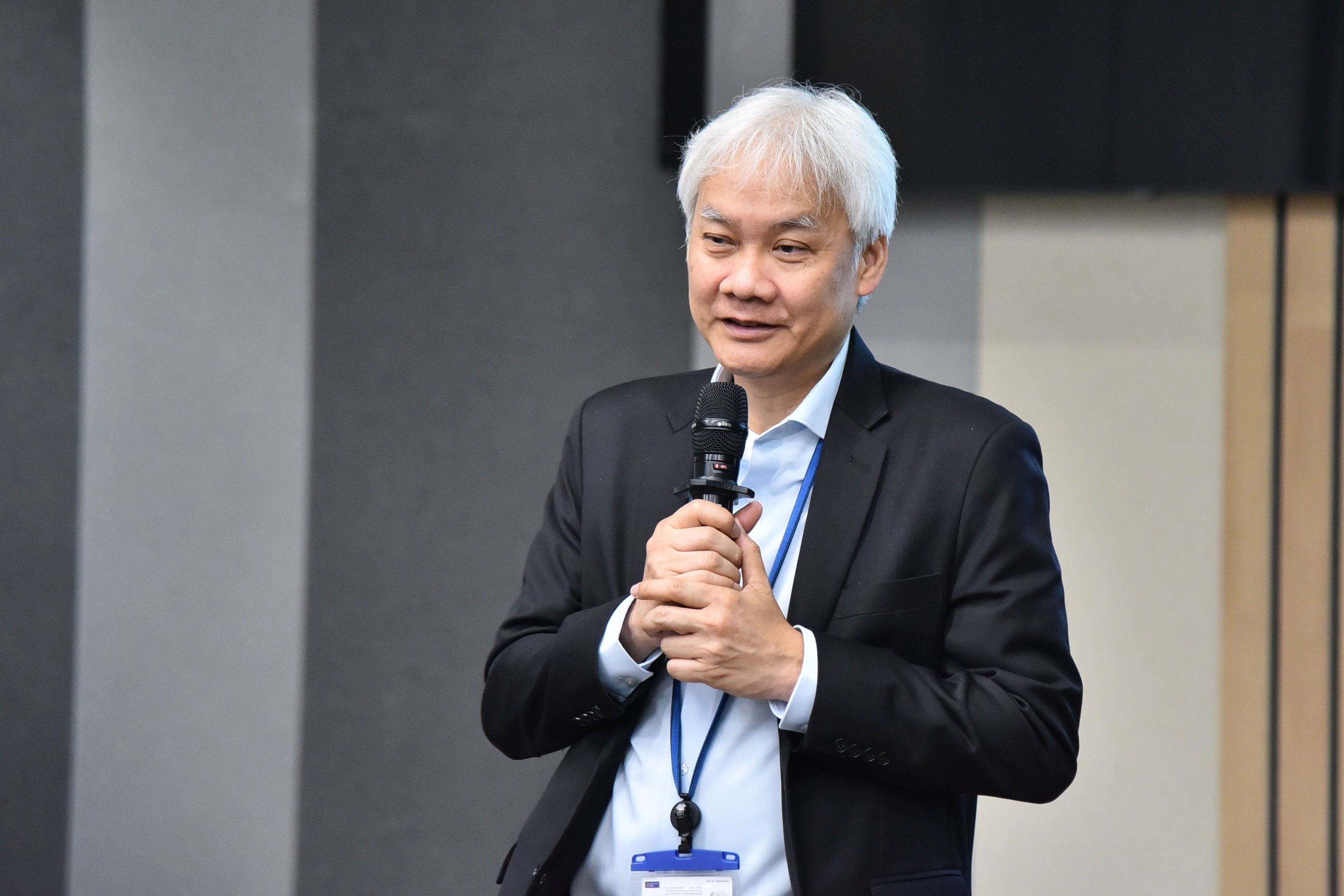 Man with white hair speaking into a microphone at a professional event.