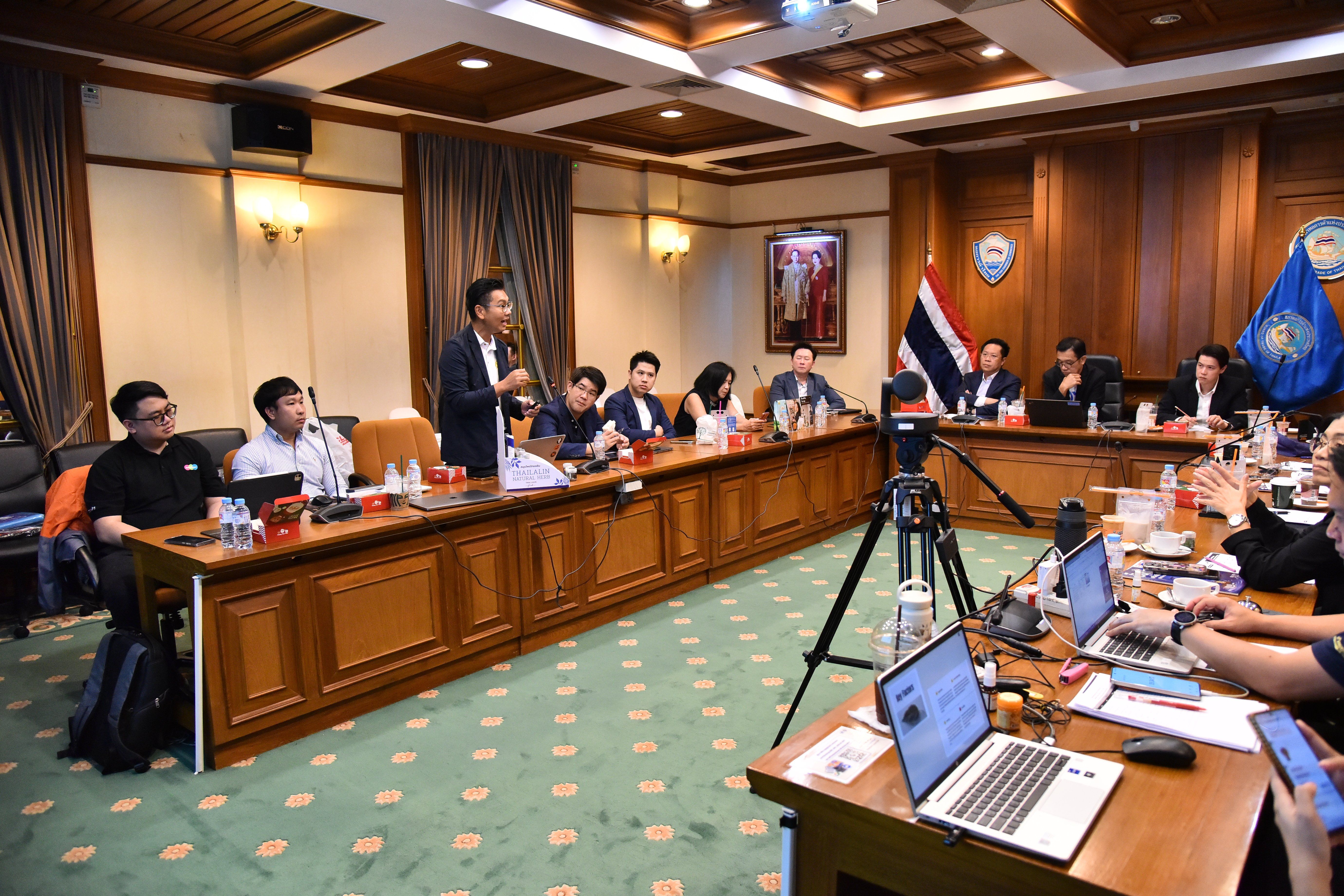 Man in suit presents to colleagues seated around a large meeting table with laptops.