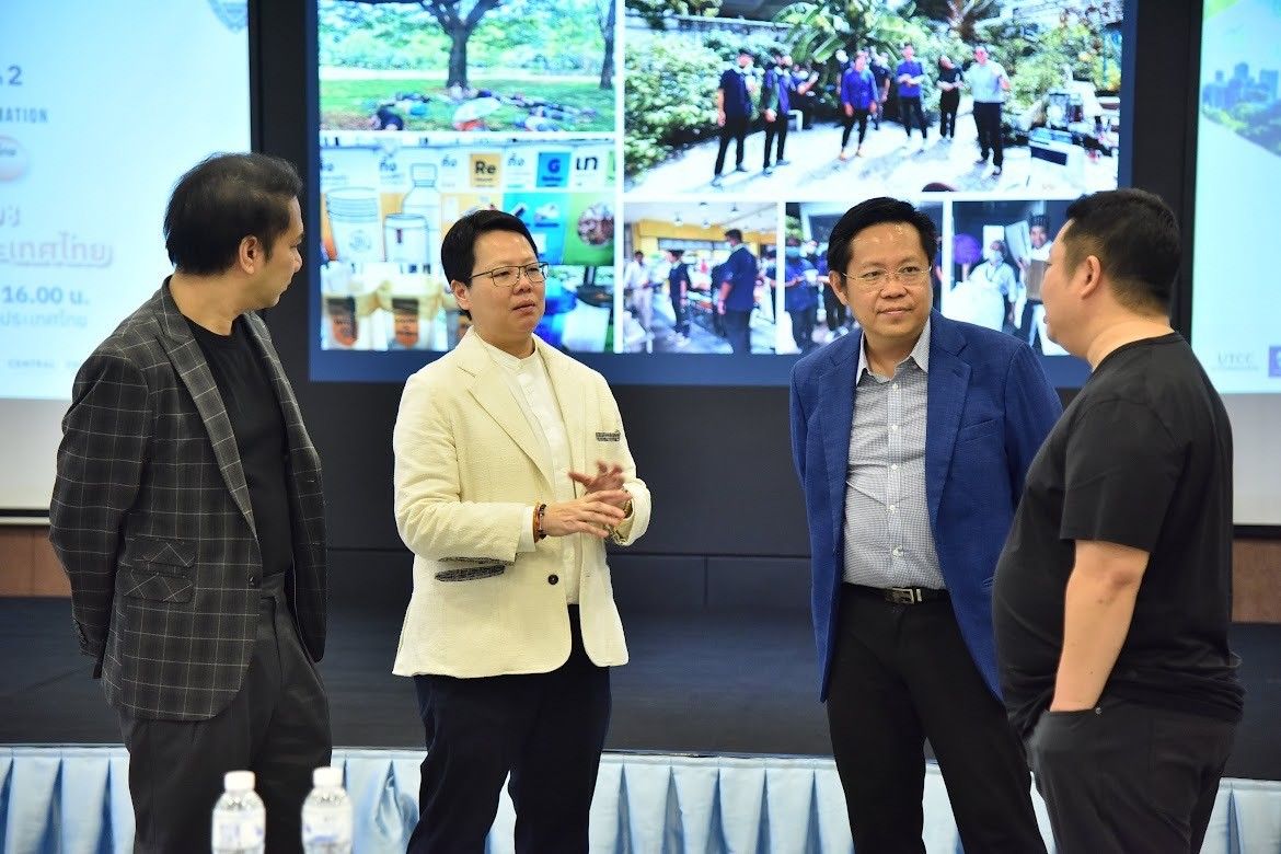 Four professional men discuss in a conference room with a large screen displaying outdoor community projects.