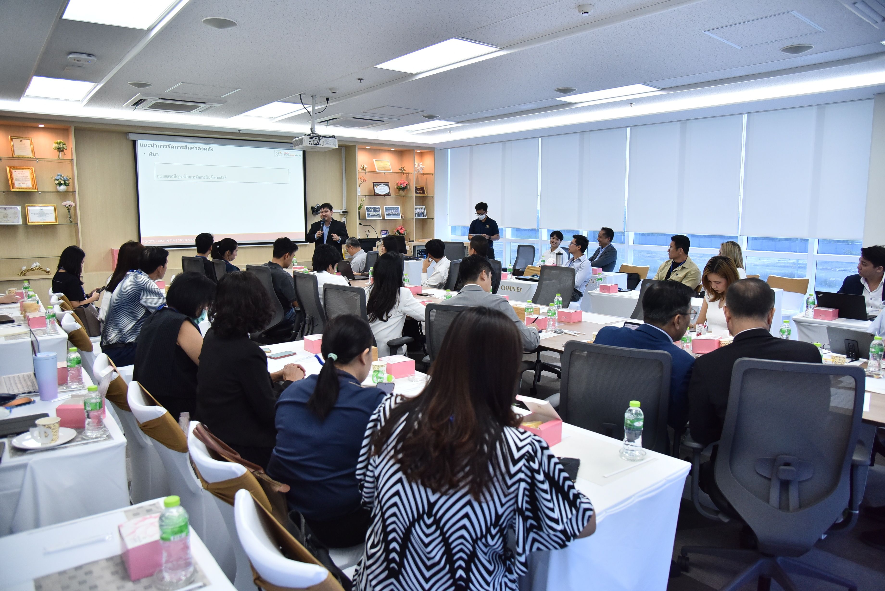 Attendees gather in a conference room for a business presentation with a projector screen.