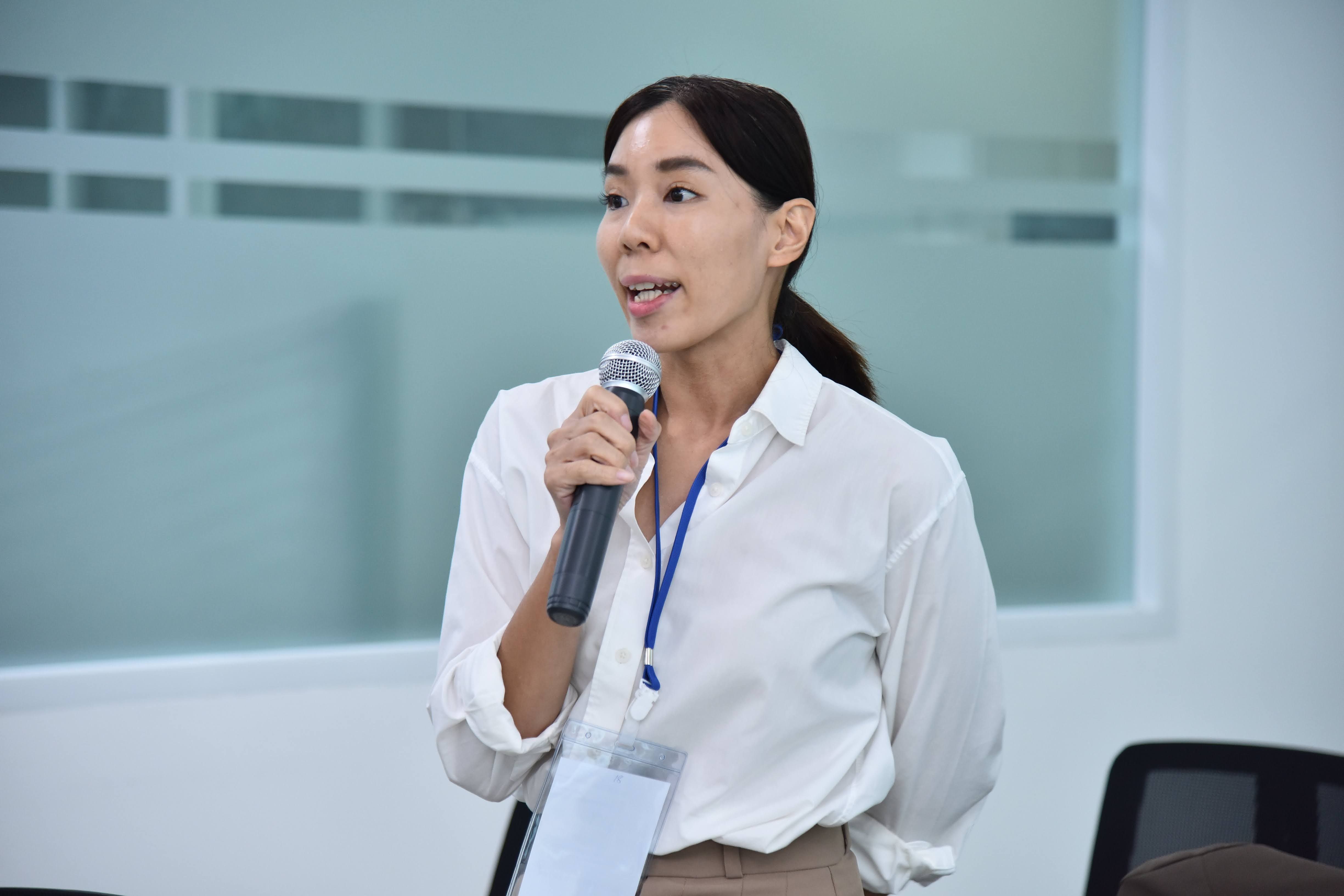 A woman in a white shirt speaks into a microphone during a presentation in an office.