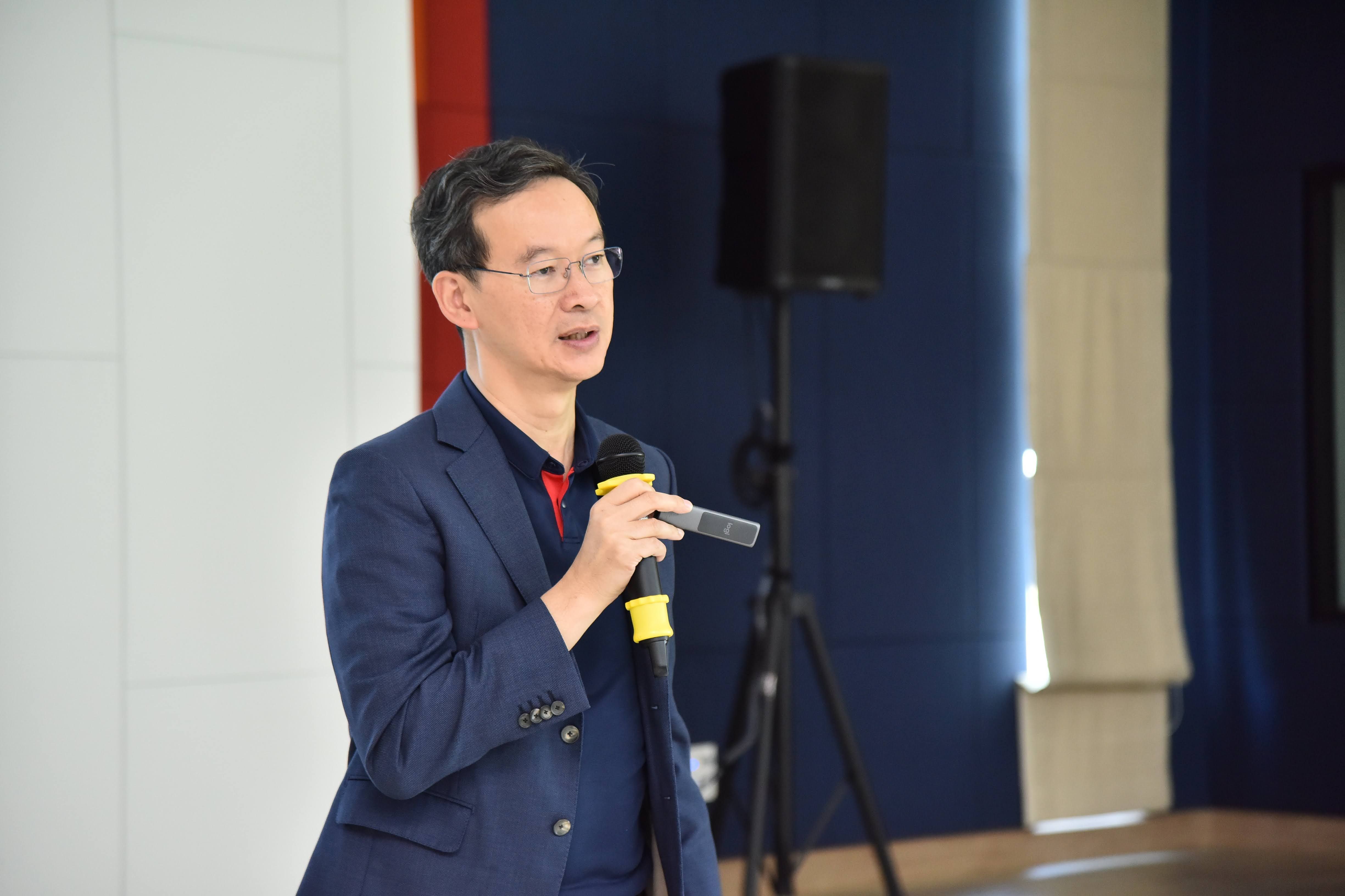 A man in a blue suit and glasses speaks into a microphone during a presentation.