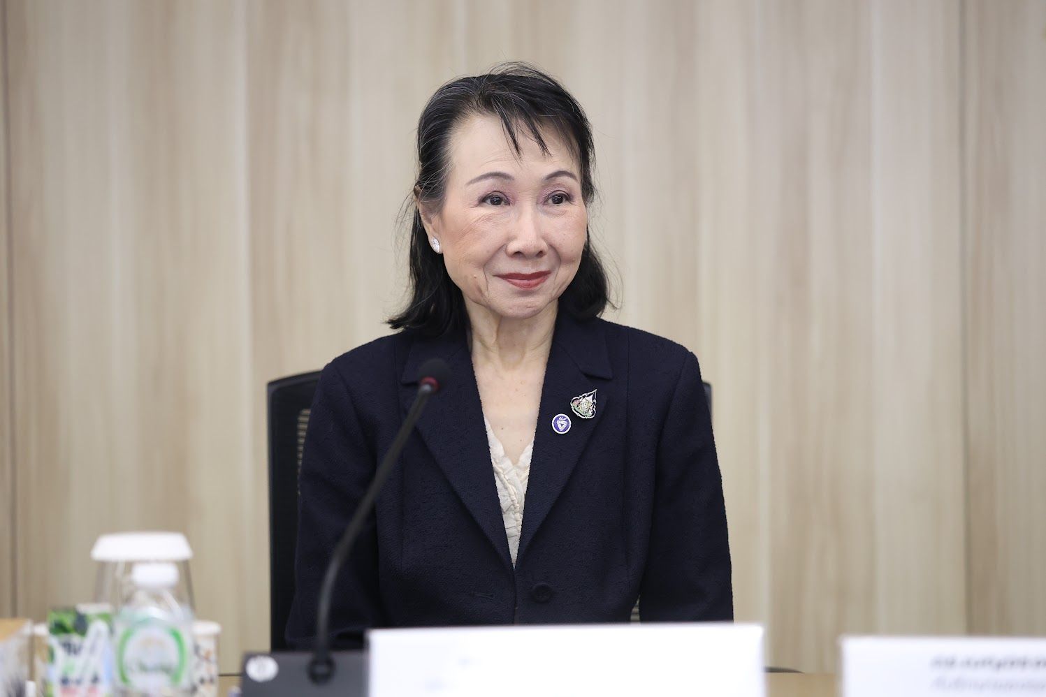 East Asian woman in dark suit jacket seated at table with microphone.