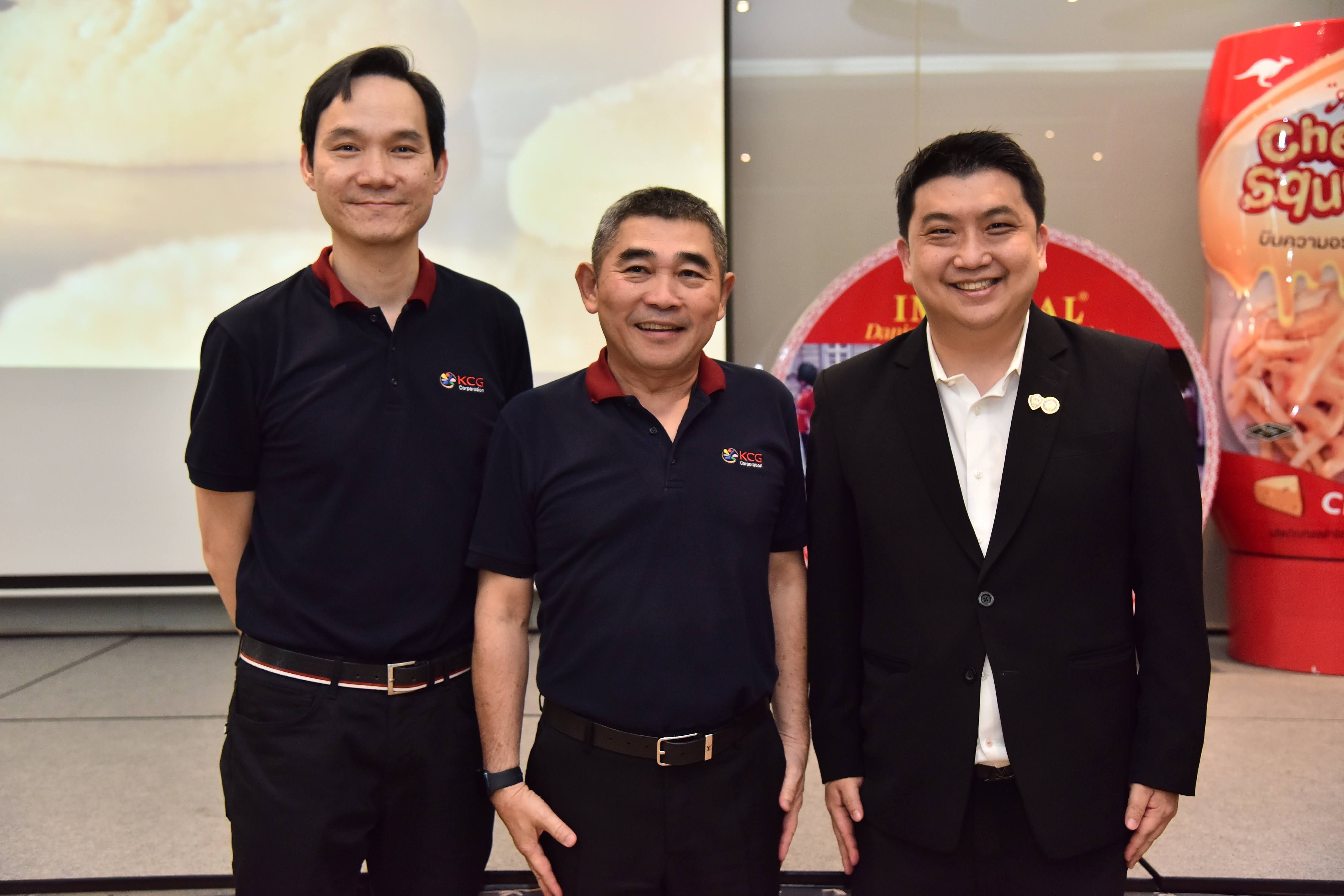 Three professional men stand by a "Cheez Squeeze" product display at an event.
