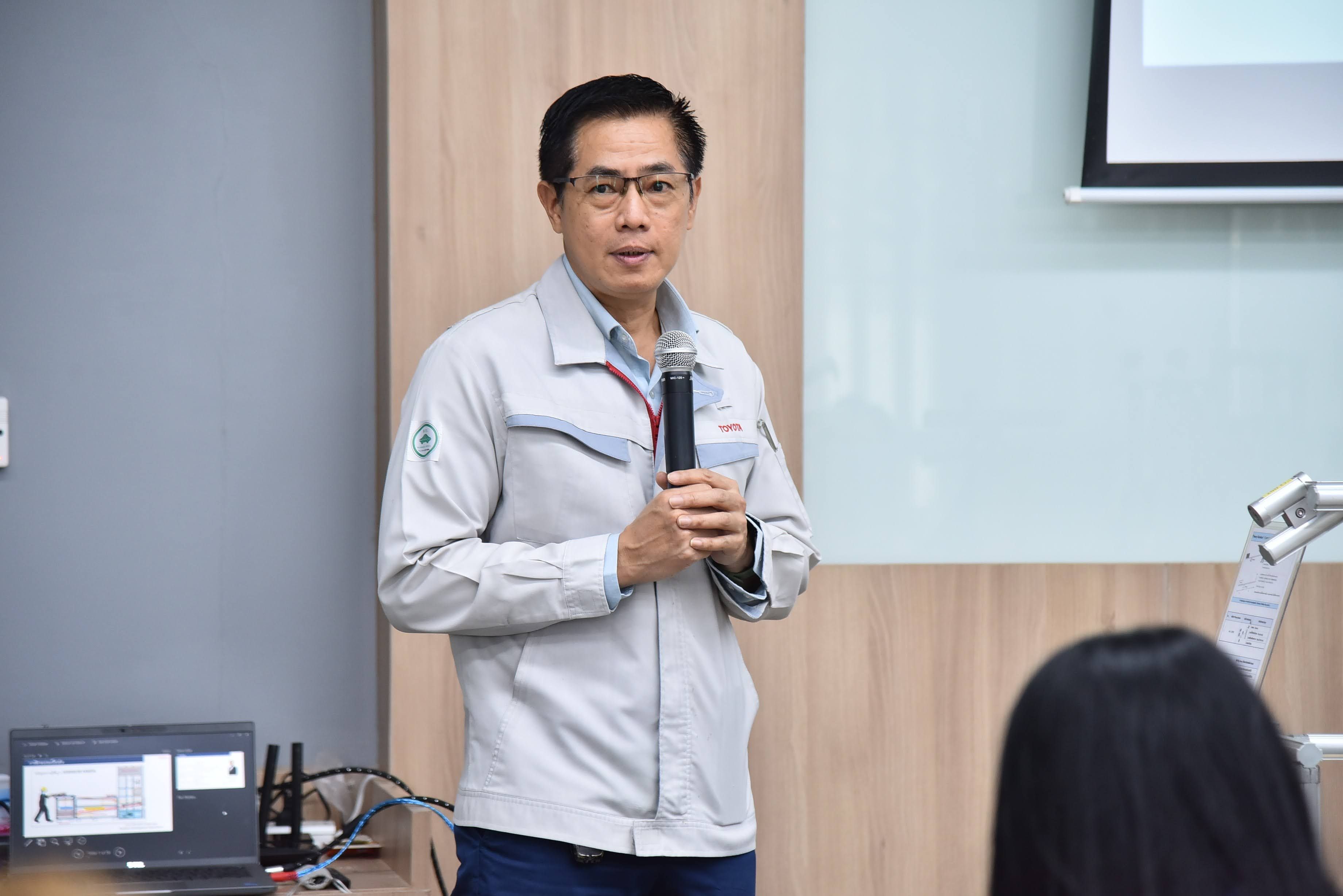 Man in grey jacket and glasses speaking into a microphone during a presentation.