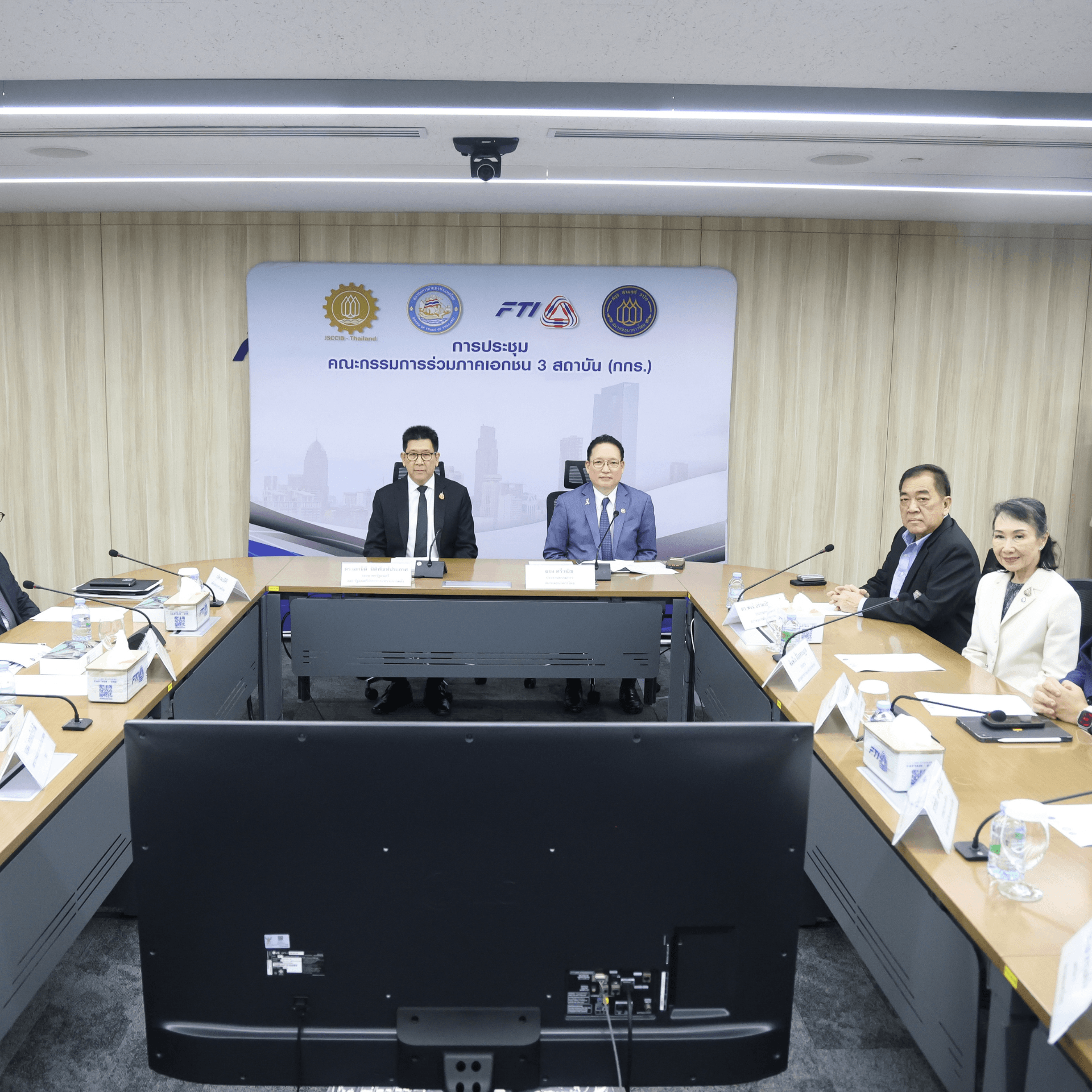 Several people attend a formal business meeting in a modern conference room with a banner.
