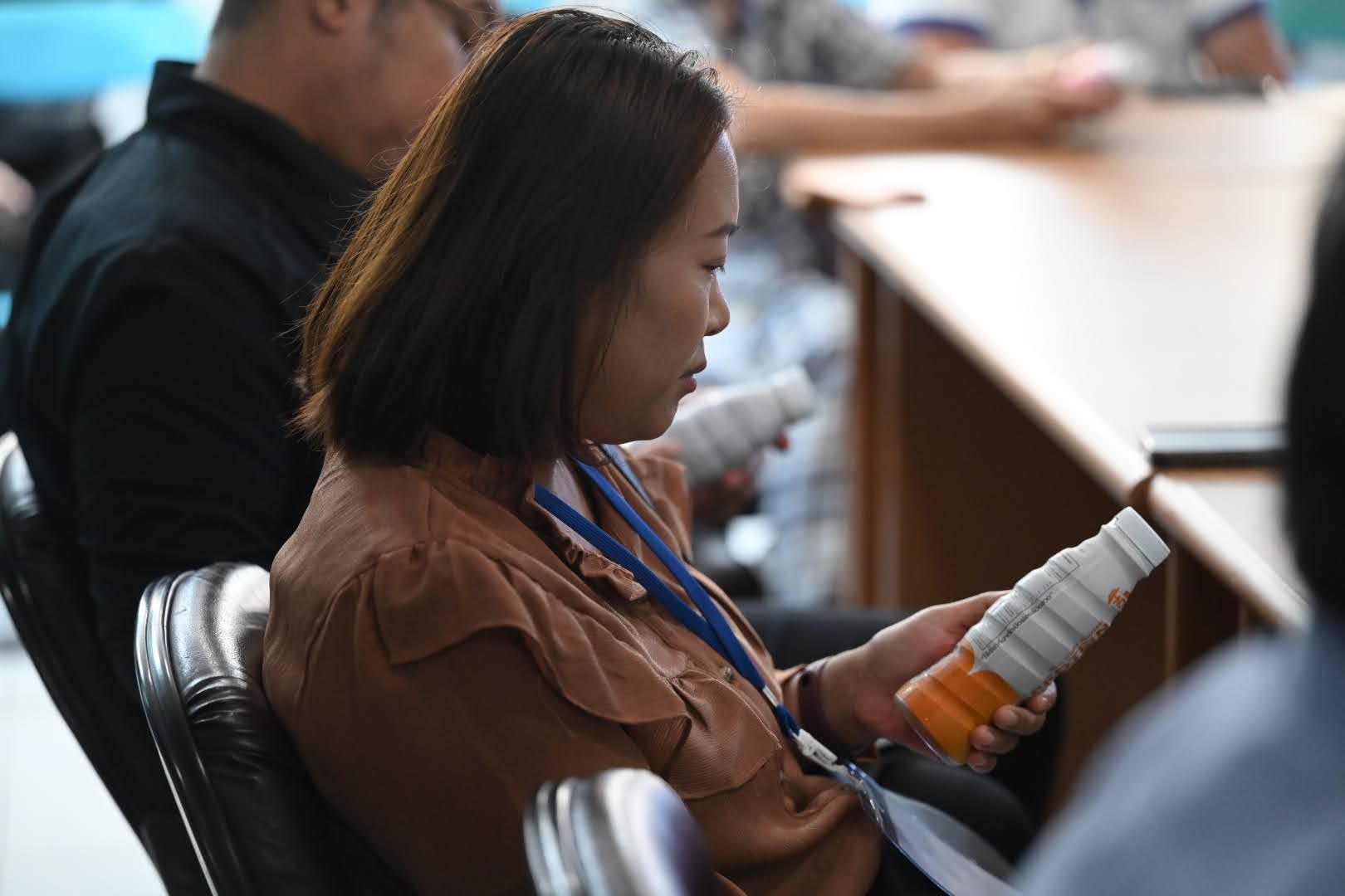 Woman in a brown shirt holding a white bottle during a meeting session.