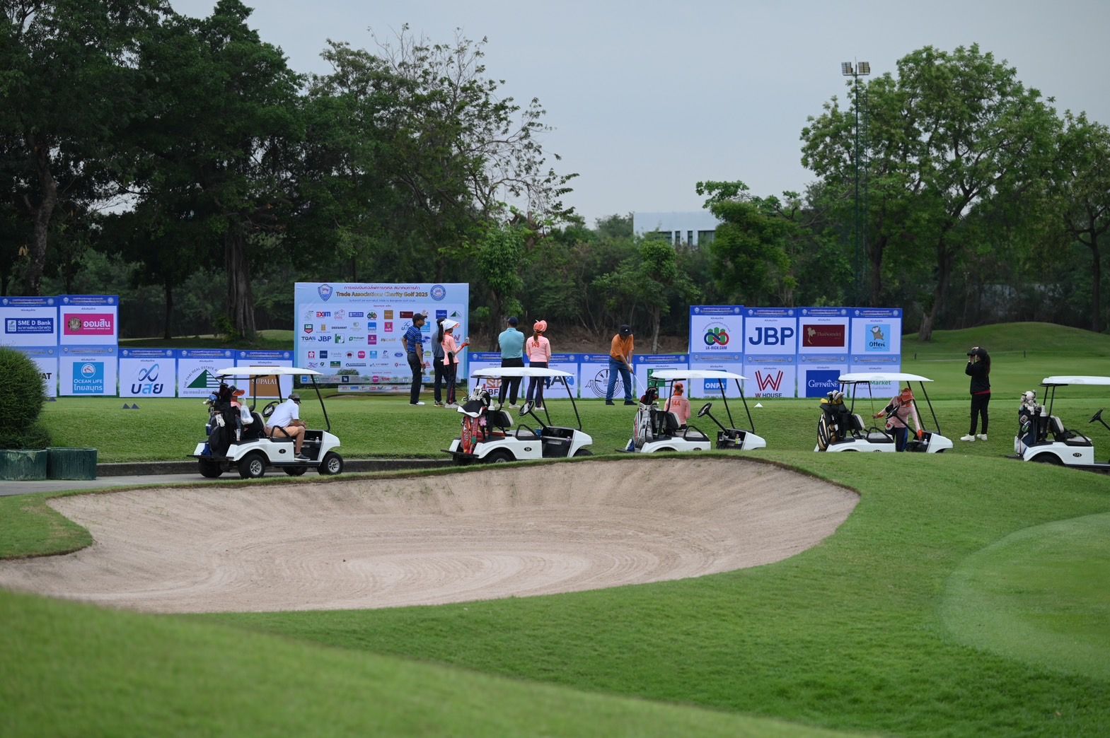 Golf carts parked on a green course near a sand bunker during an event.