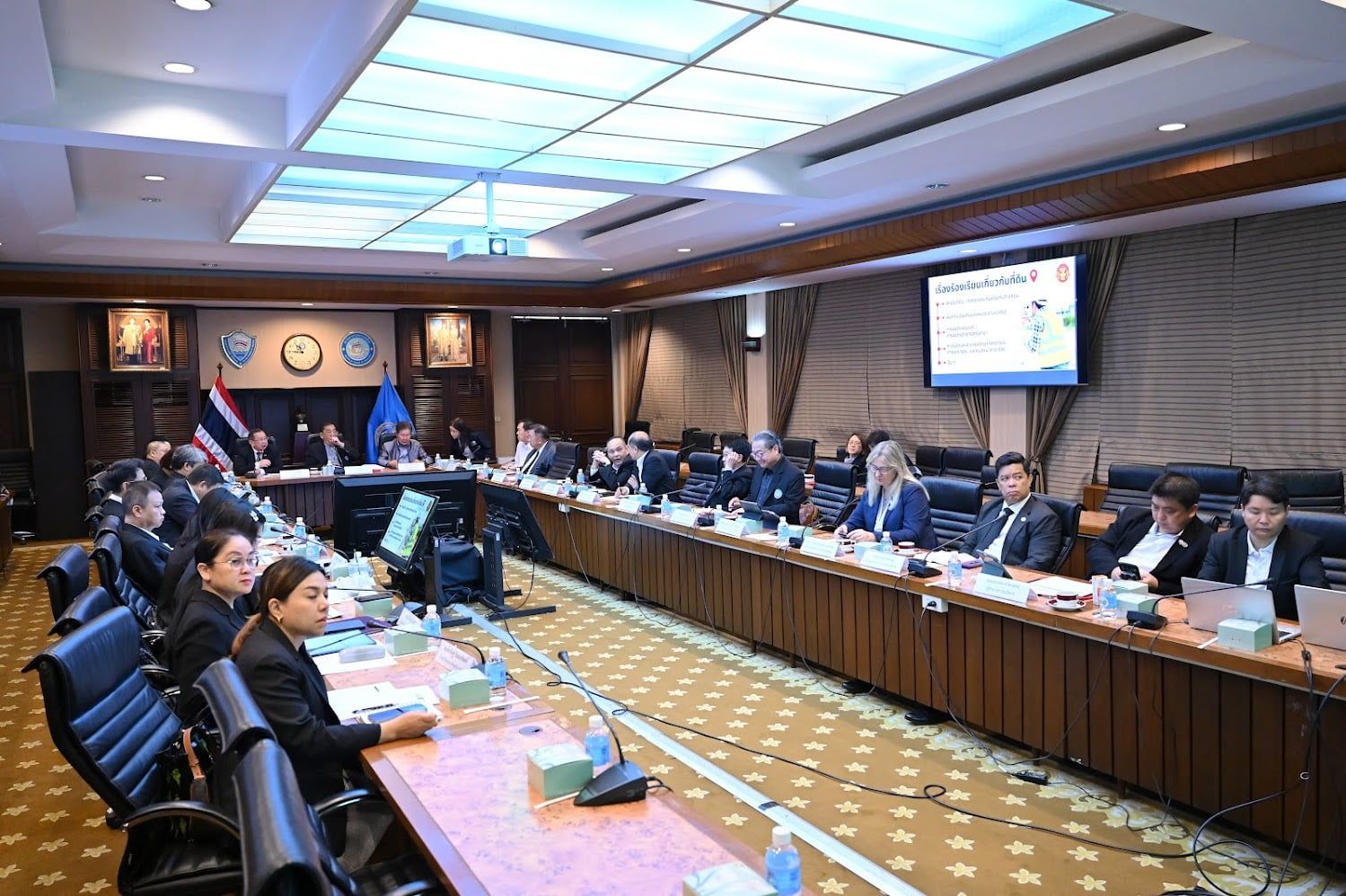 Professionals attend a formal meeting around a long conference table with a presentation screen.