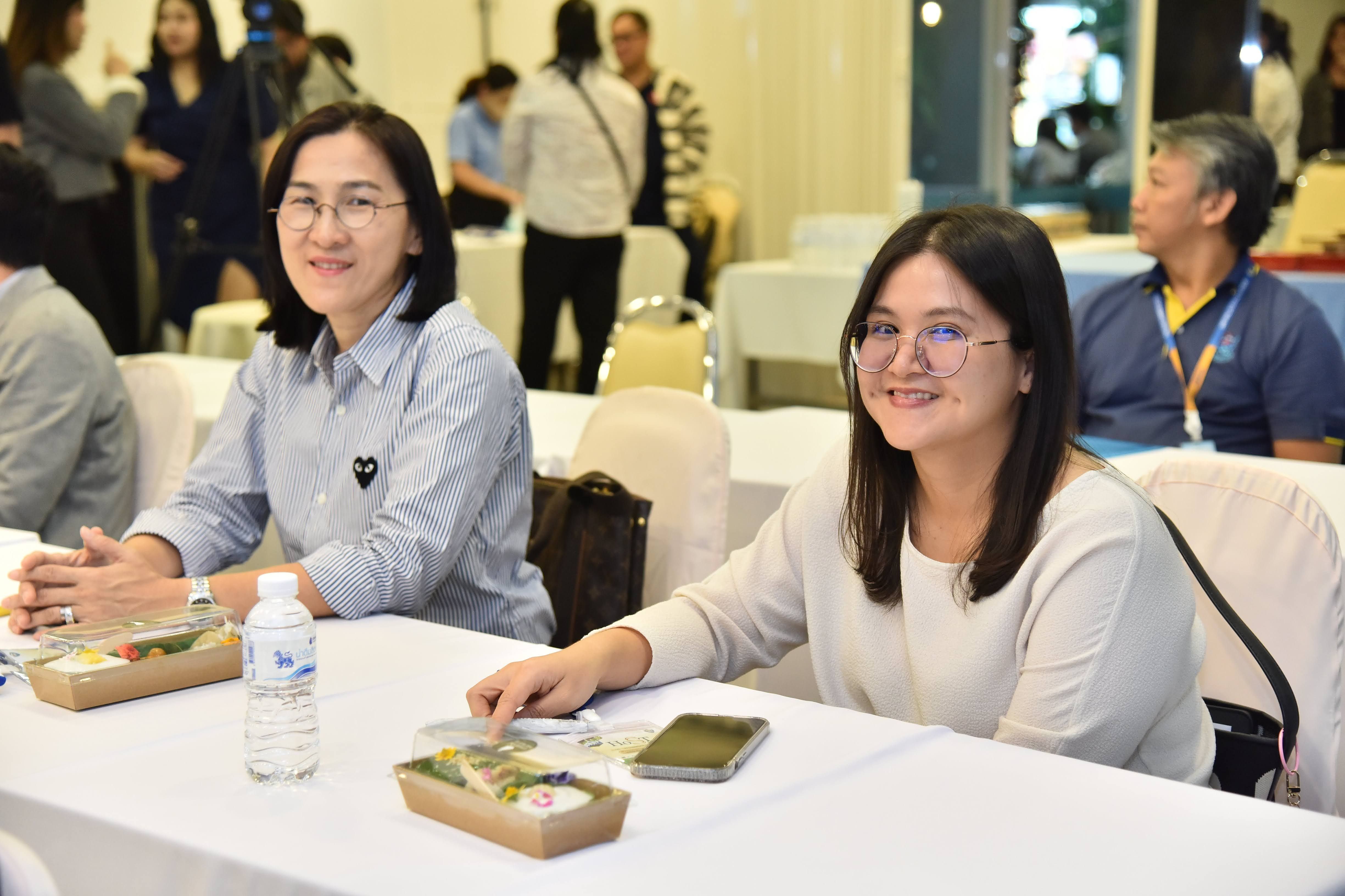 Two smiling women seated at a table with food and drinks at an event.