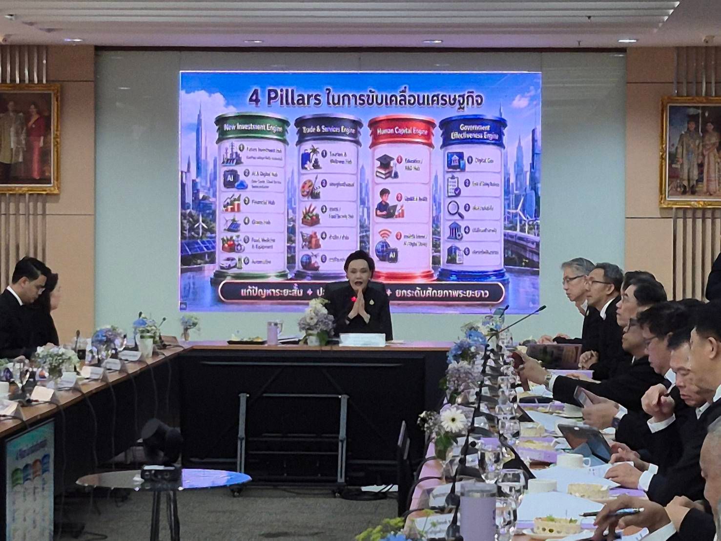 Man presents '4 Pillars' graphic to colleagues during a formal conference meeting.