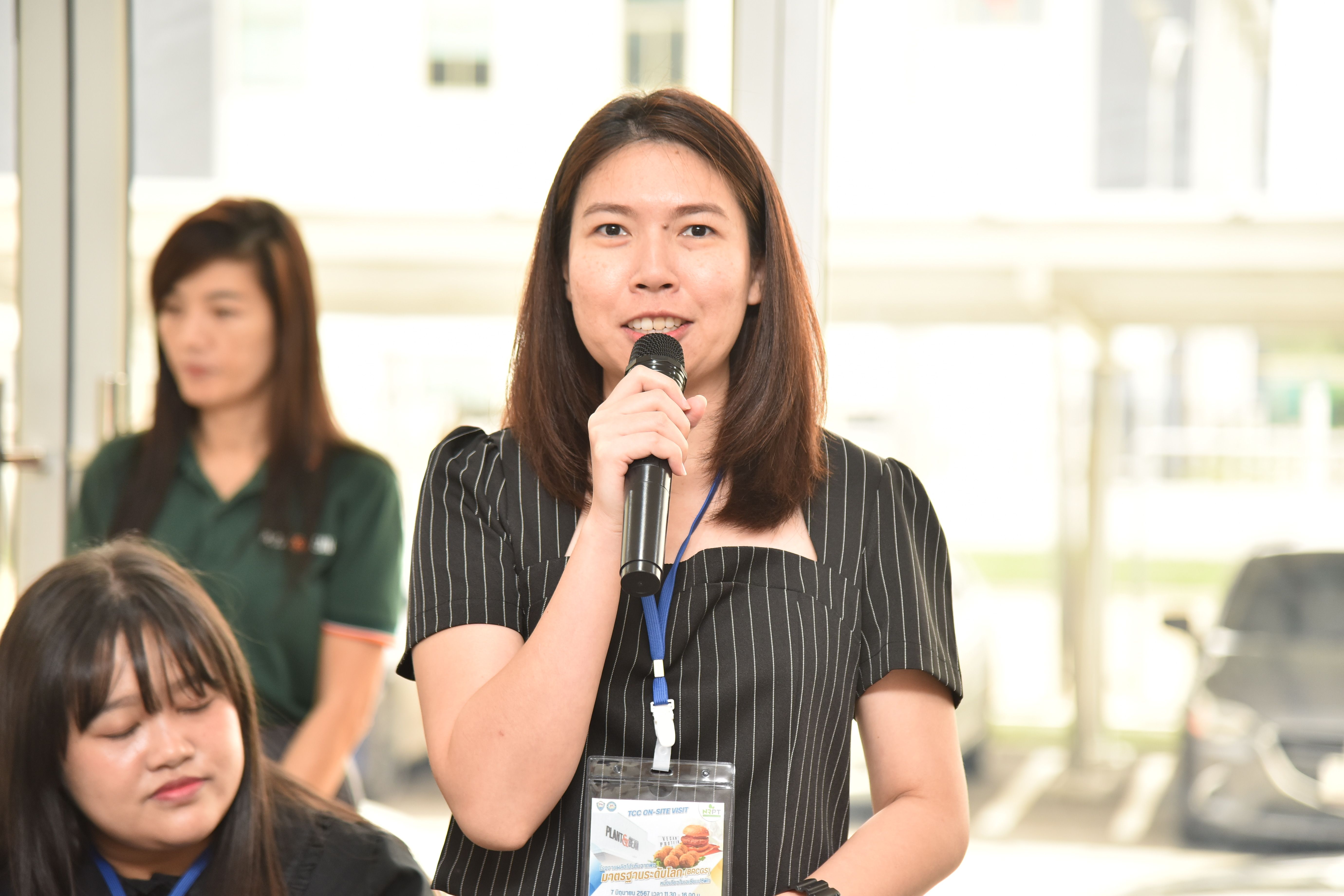 Woman speaking into a microphone at an indoor event with a lanyard.