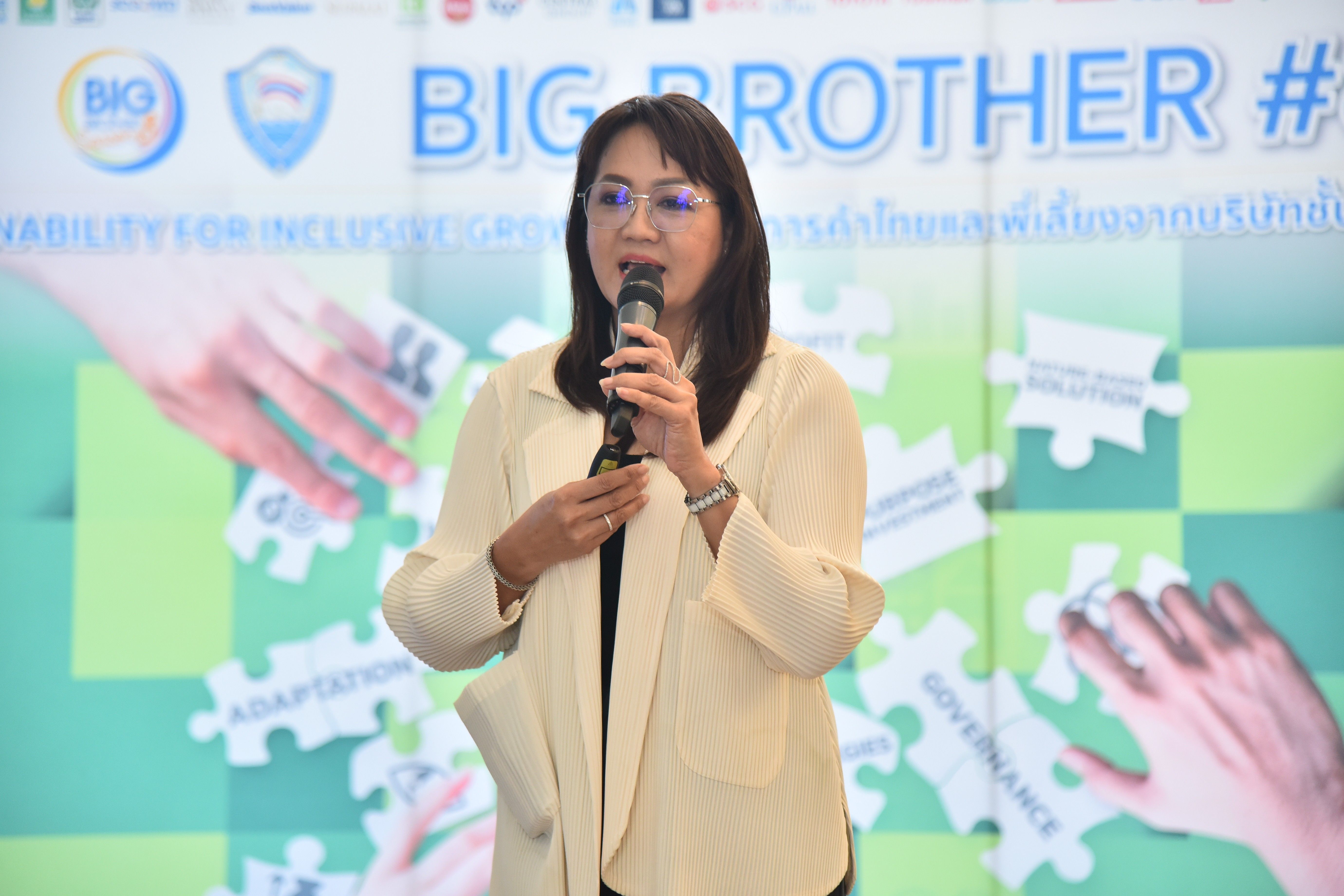 Woman speaking into microphone at event with 'BIG BROTHER' and inclusion-themed backdrop.