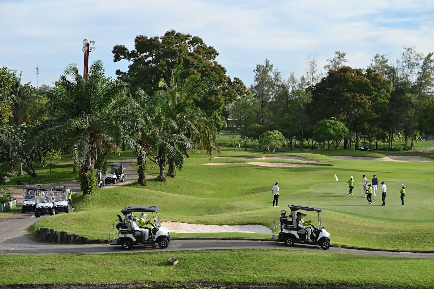 Golfers play on a lush green course with palm trees and golf carts.