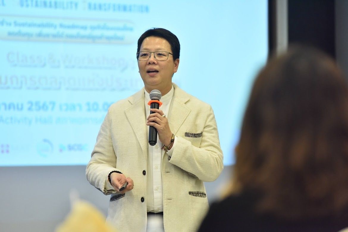 Man in glasses and a light suit speaks into a microphone during a presentation.