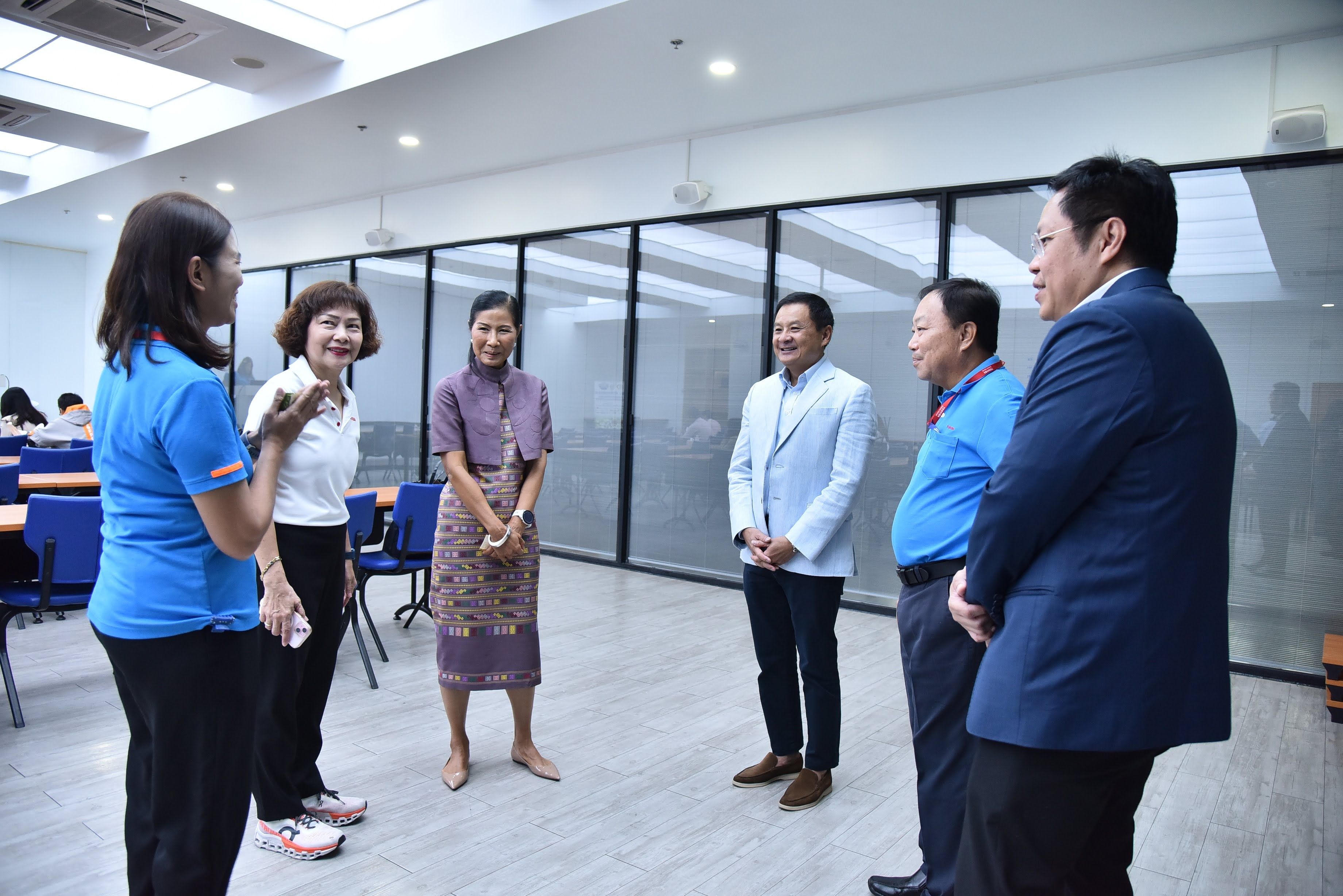 Six people, including a woman in traditional Thai dress, conversing in a modern office.
