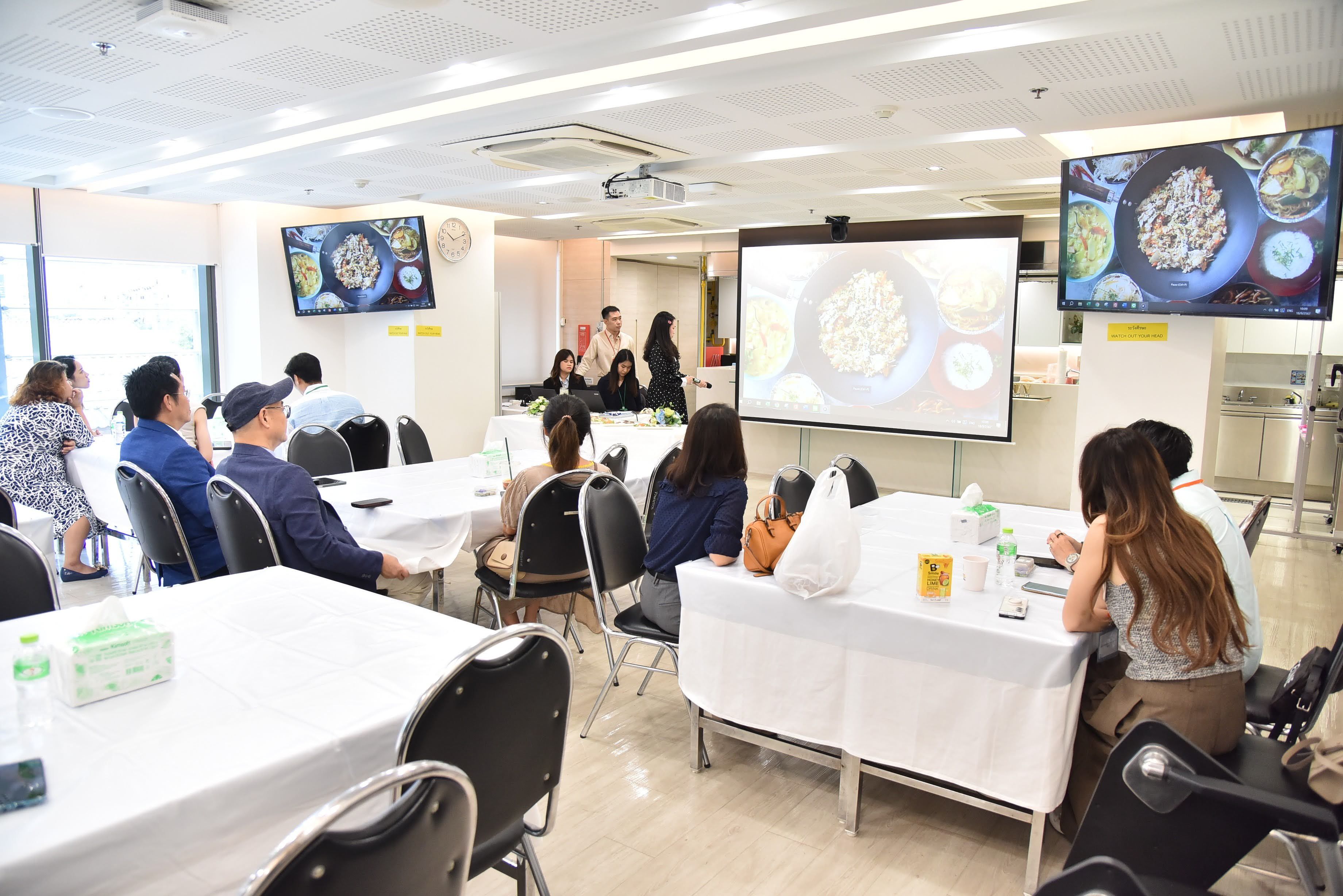 Attendees watch a cooking demonstration featuring food images on a large projector screen.