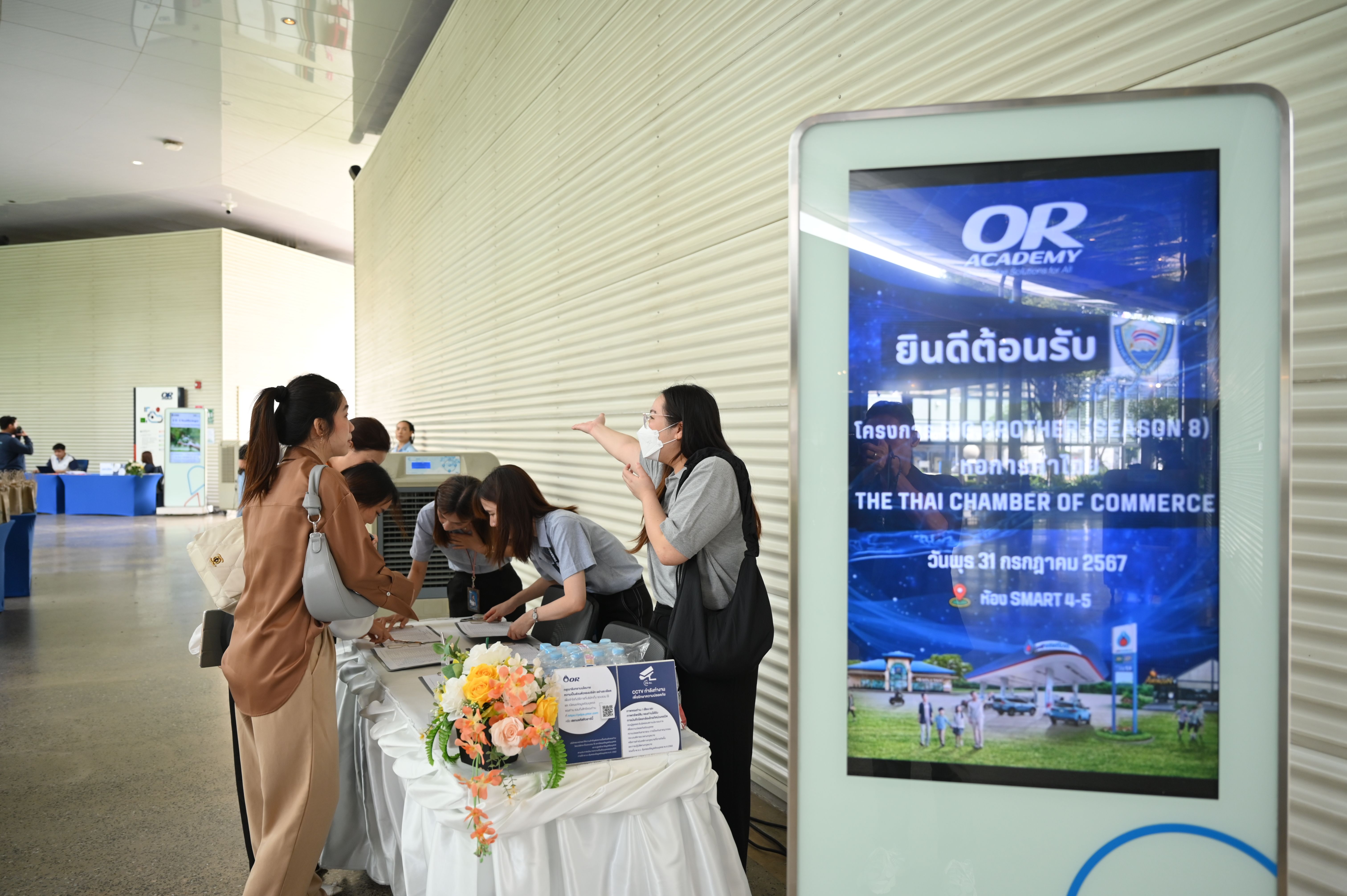 People gather at a registration table next to a large digital display for an event.