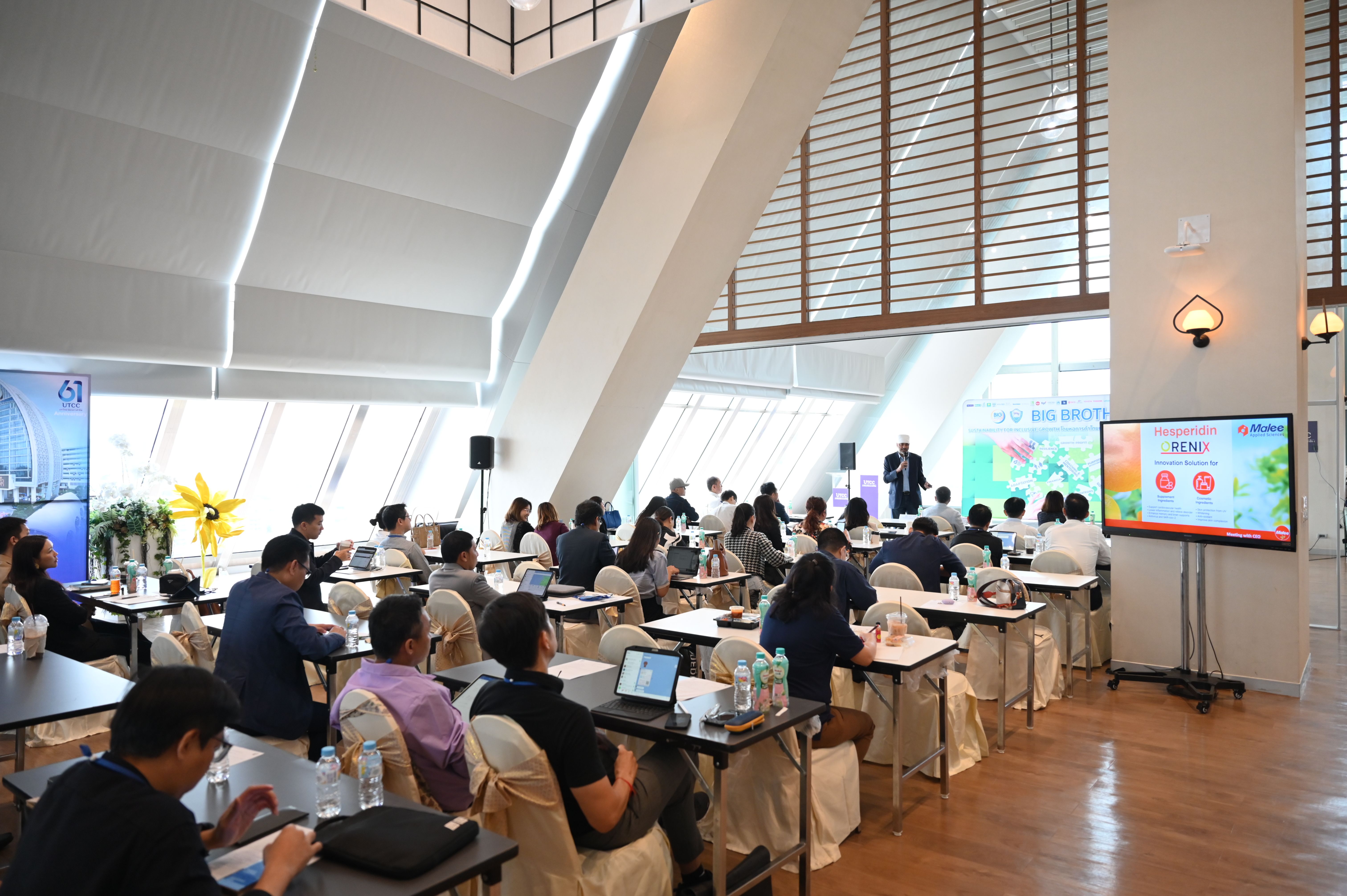 Attendees observe a presentation in a bright, modern conference room with a large screen.