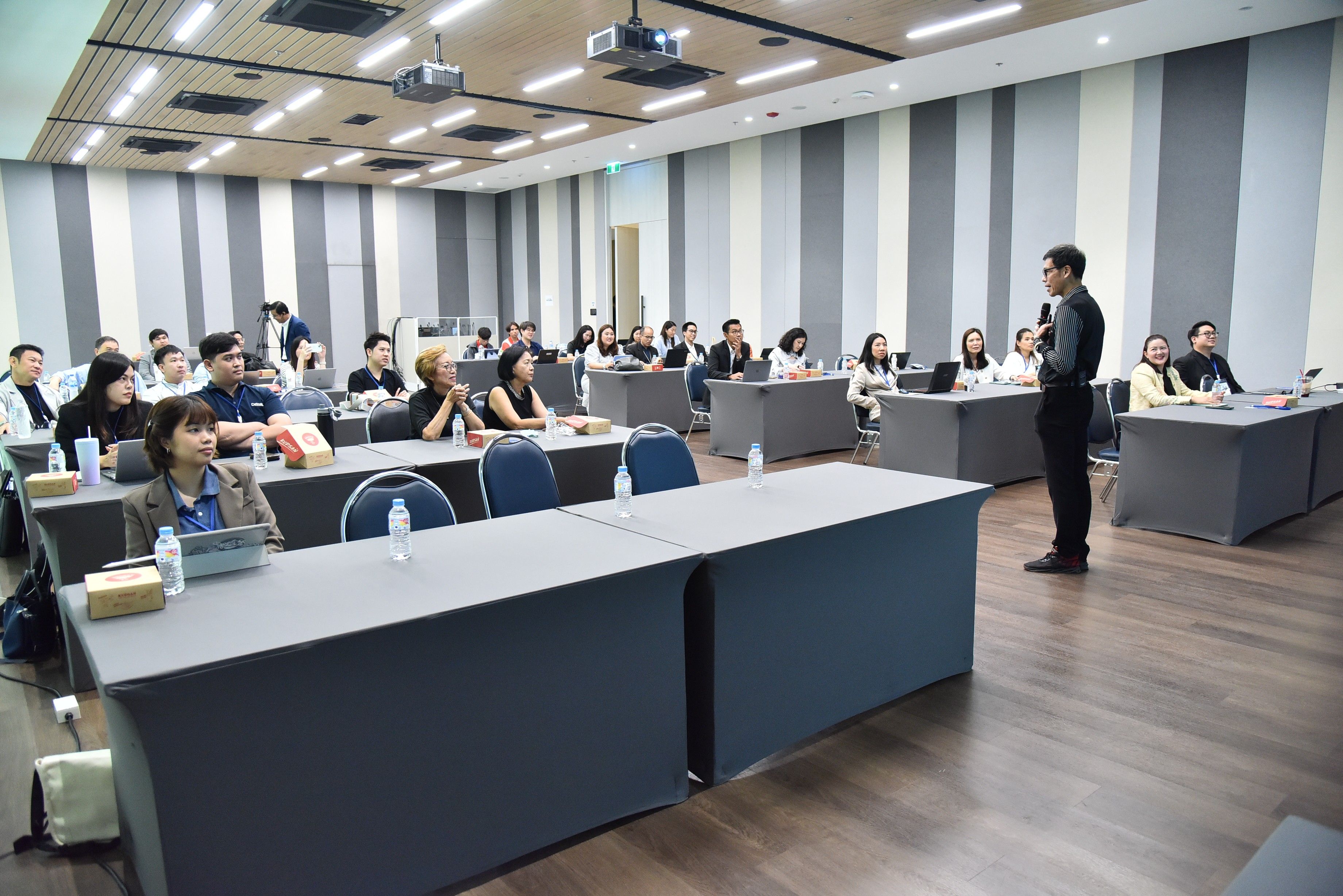 Man presents to an attentive audience in a modern conference room with projector.