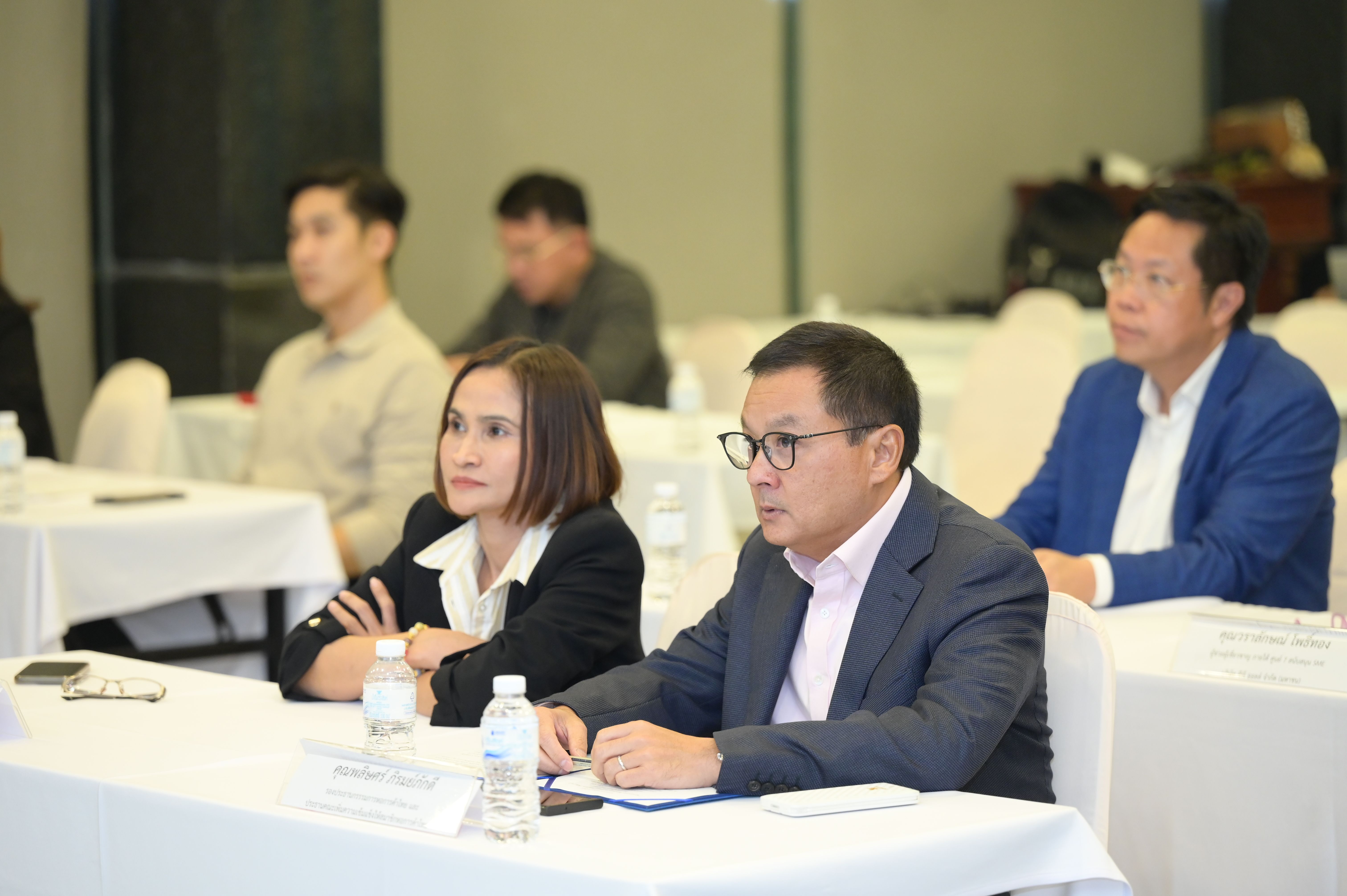 Professionals in business attire attentively listen at a conference table with water bottles and papers.