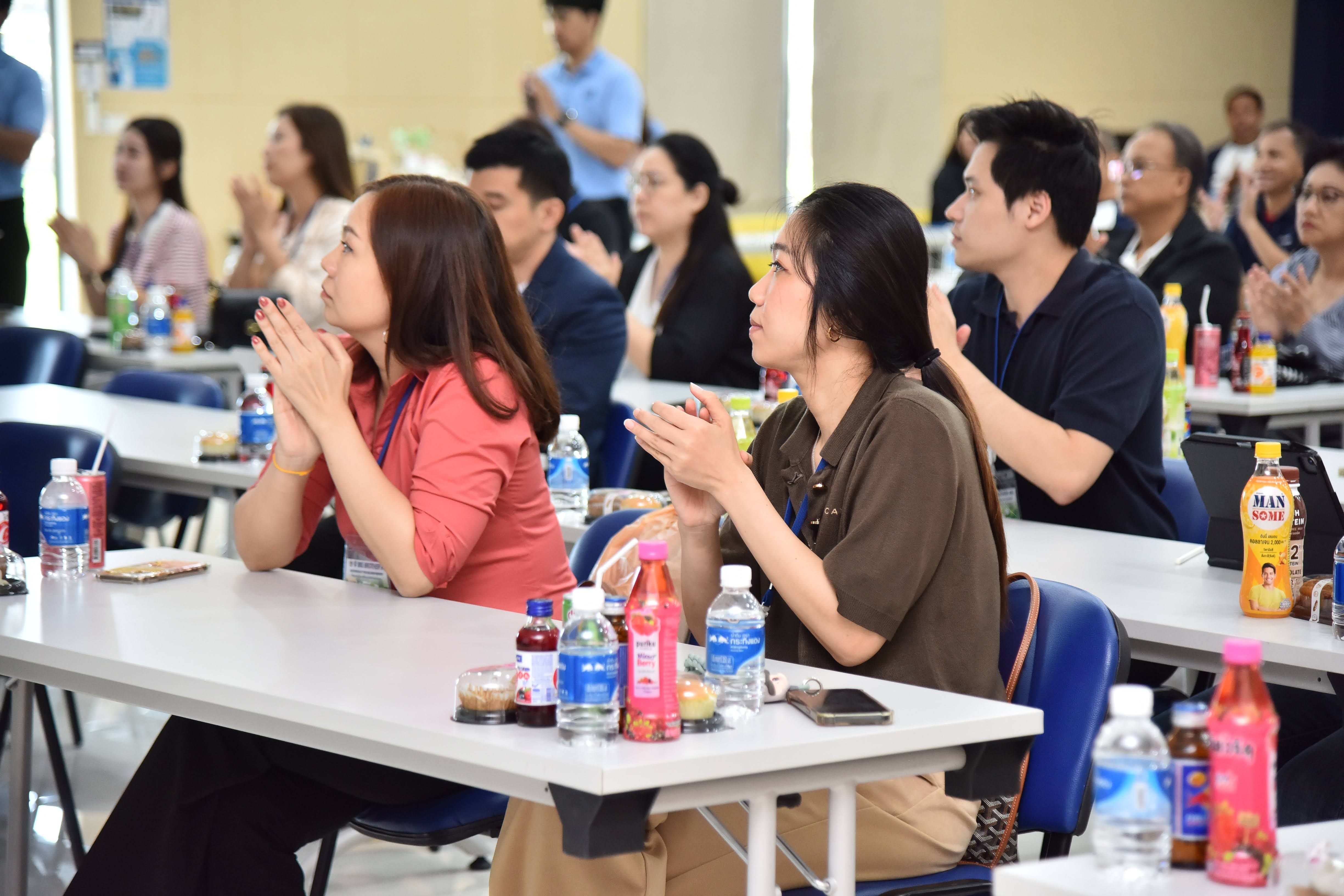 Group of attendees clapping enthusiastically while seated at white tables during an indoor event.