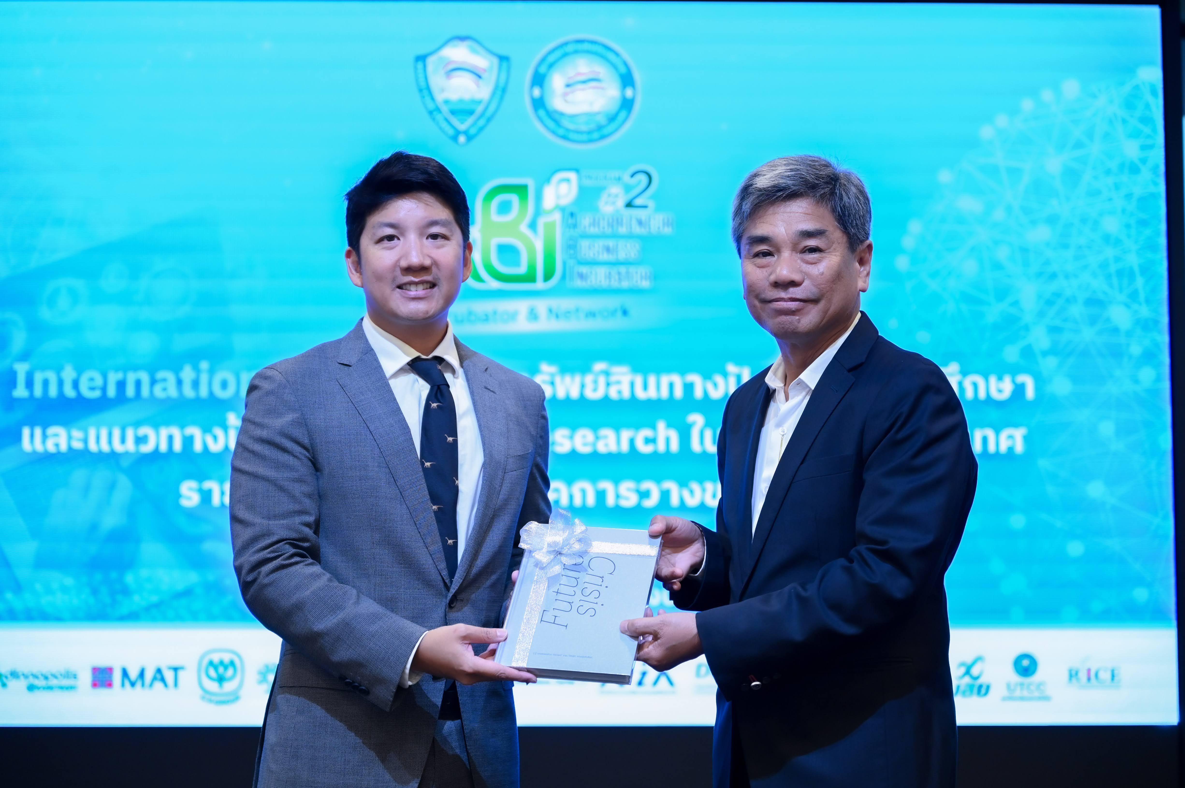 Two men exchange a silver-wrapped award on stage at an international research event.