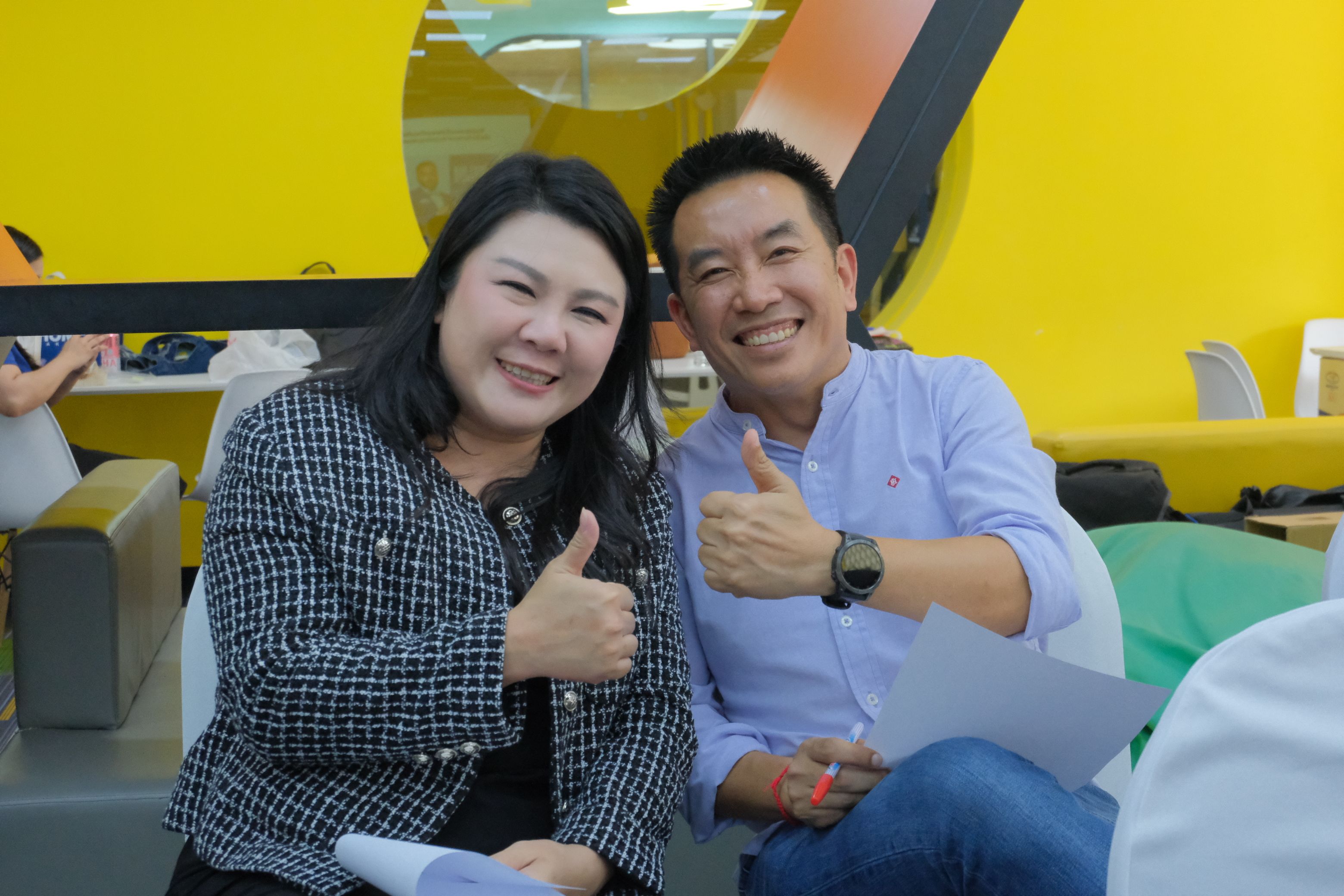 Two smiling professionals giving thumbs up in a bright, modern setting.