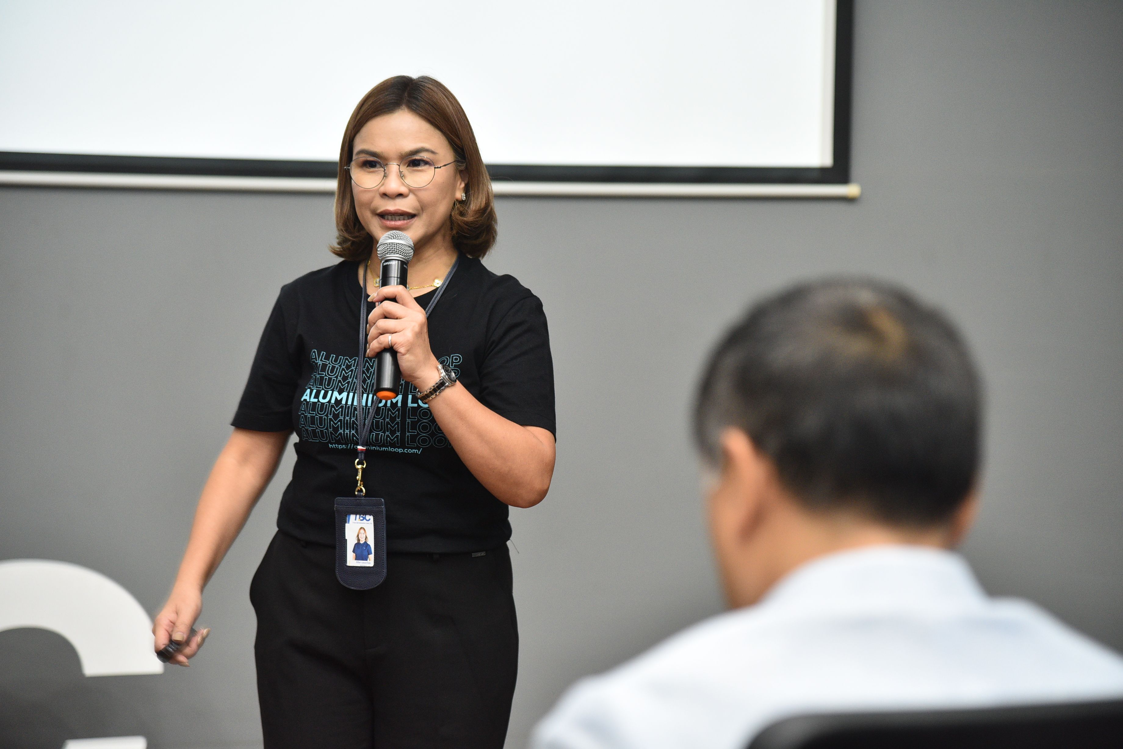 A woman with short hair speaks into a microphone during a presentation.
