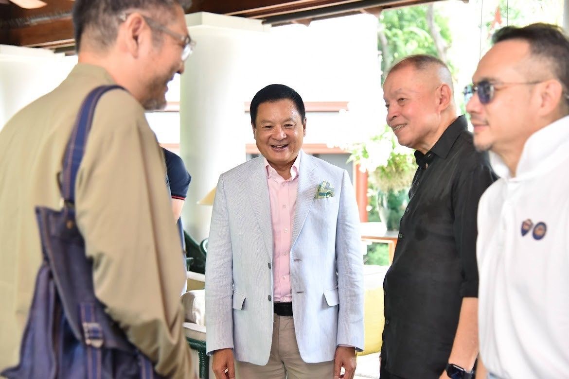 A man in a light suit smiles among three other men conversing at a social gathering.