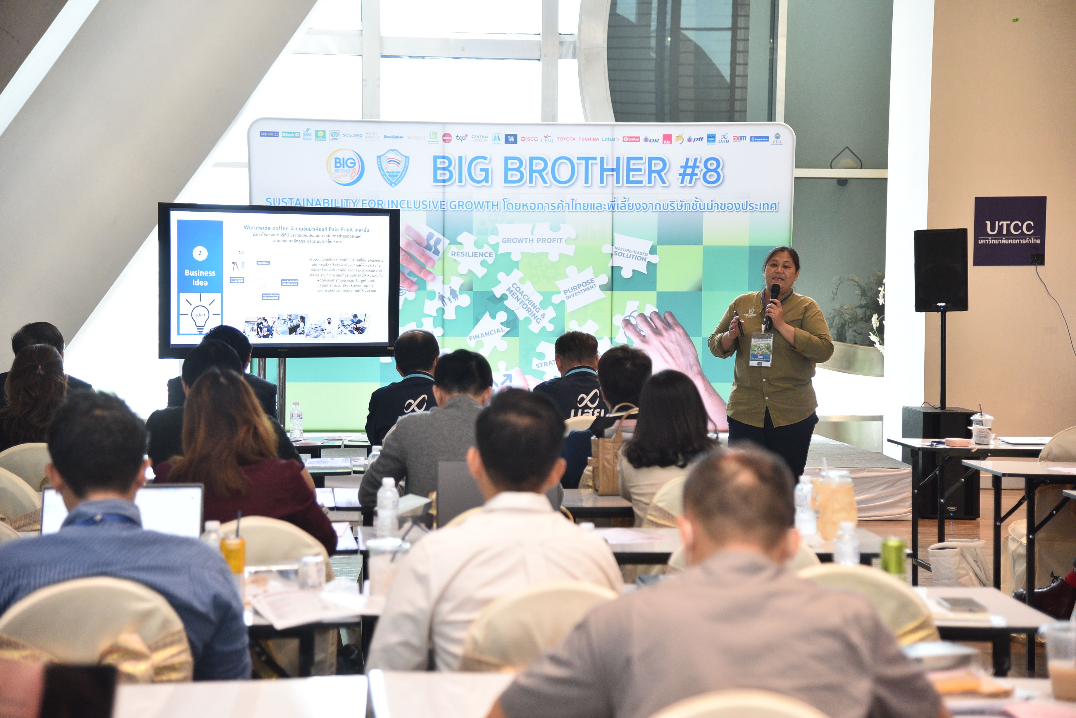 A man presents to an audience, with screens displaying 'BIG BROTHER #B' and presentation slides.