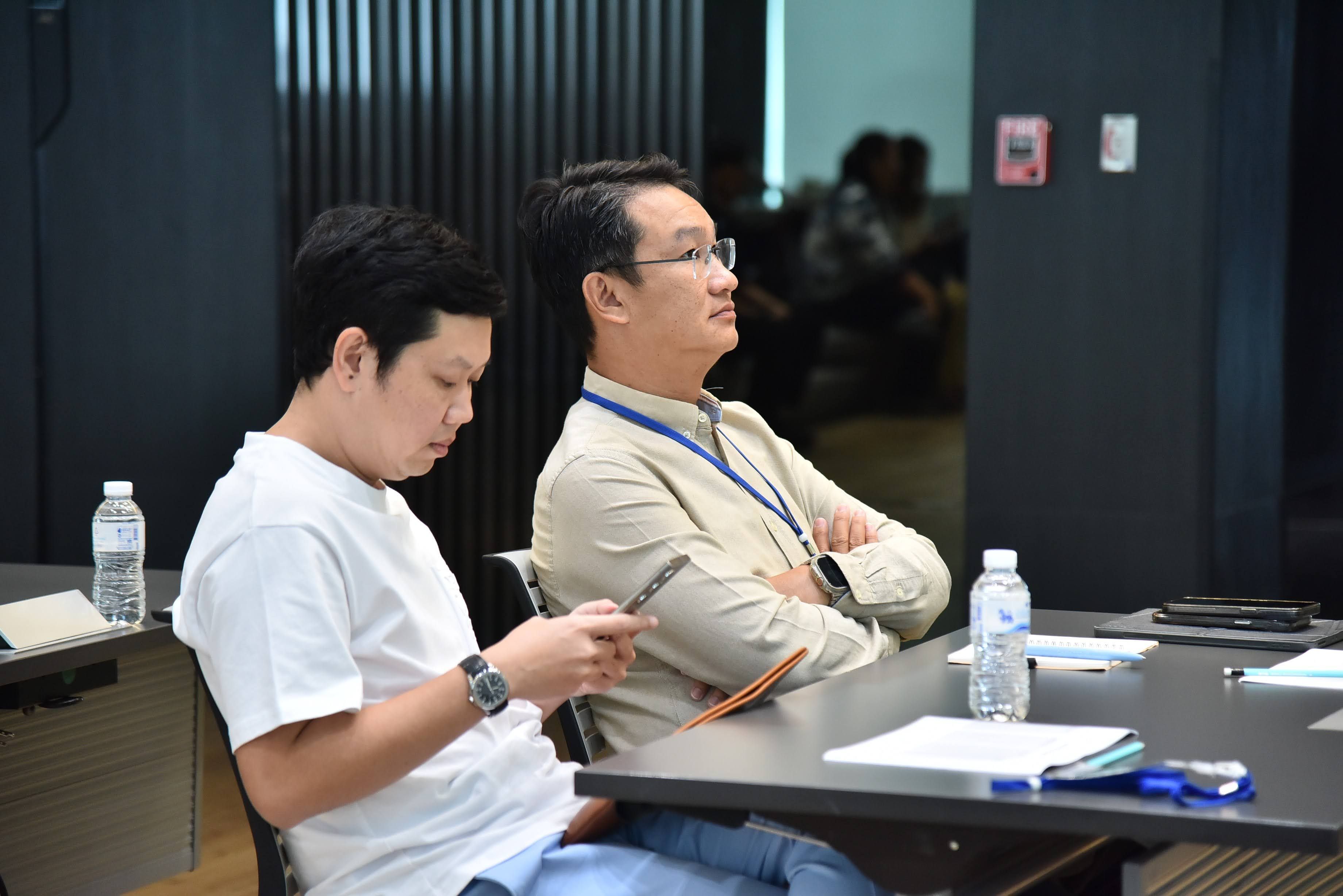 Two men, one looking at his phone, another listening intently in a modern meeting setting.