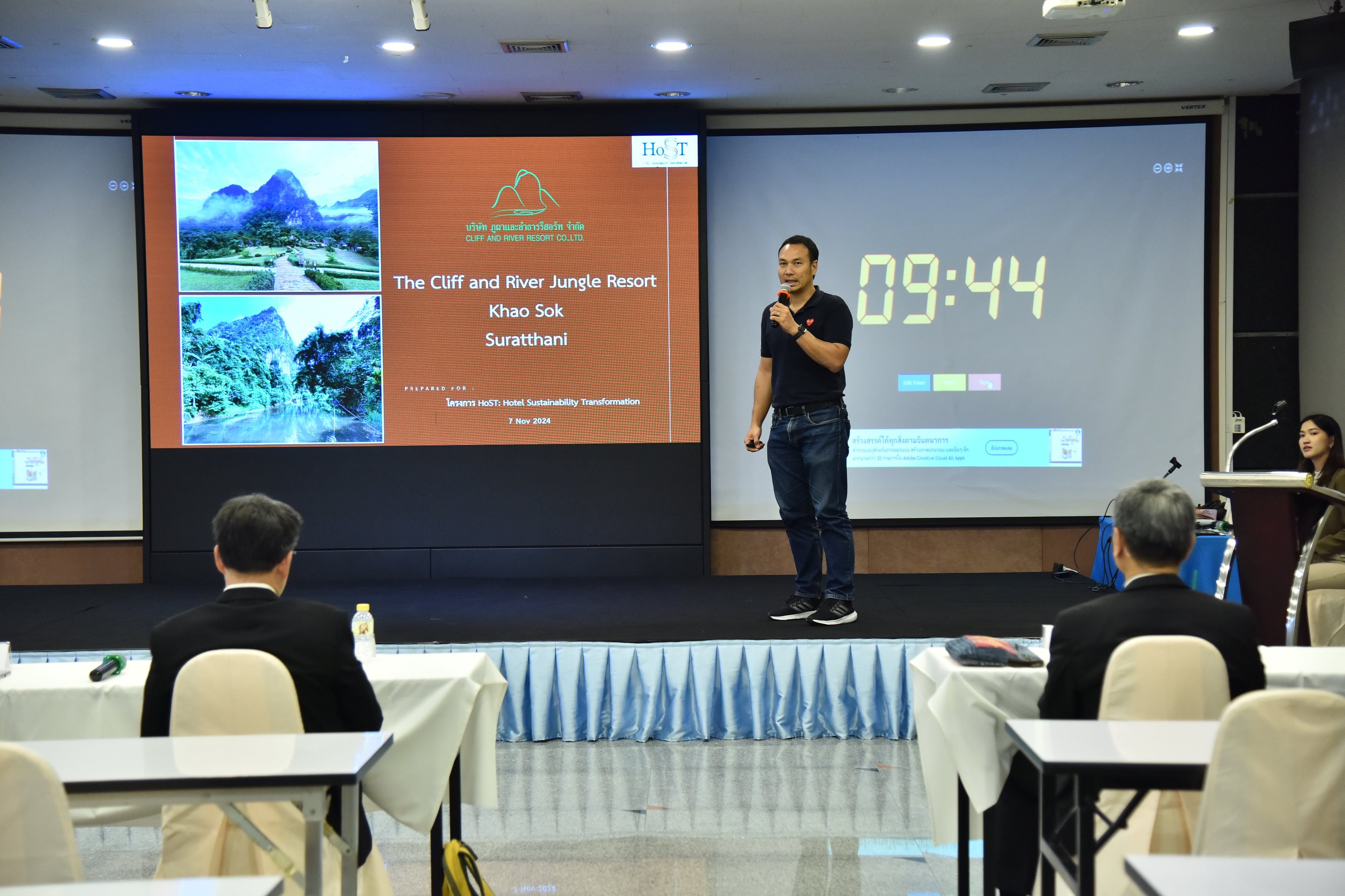 Man presents 'Khao Lak' tourism info on screen with digital timer for conference attendees.
