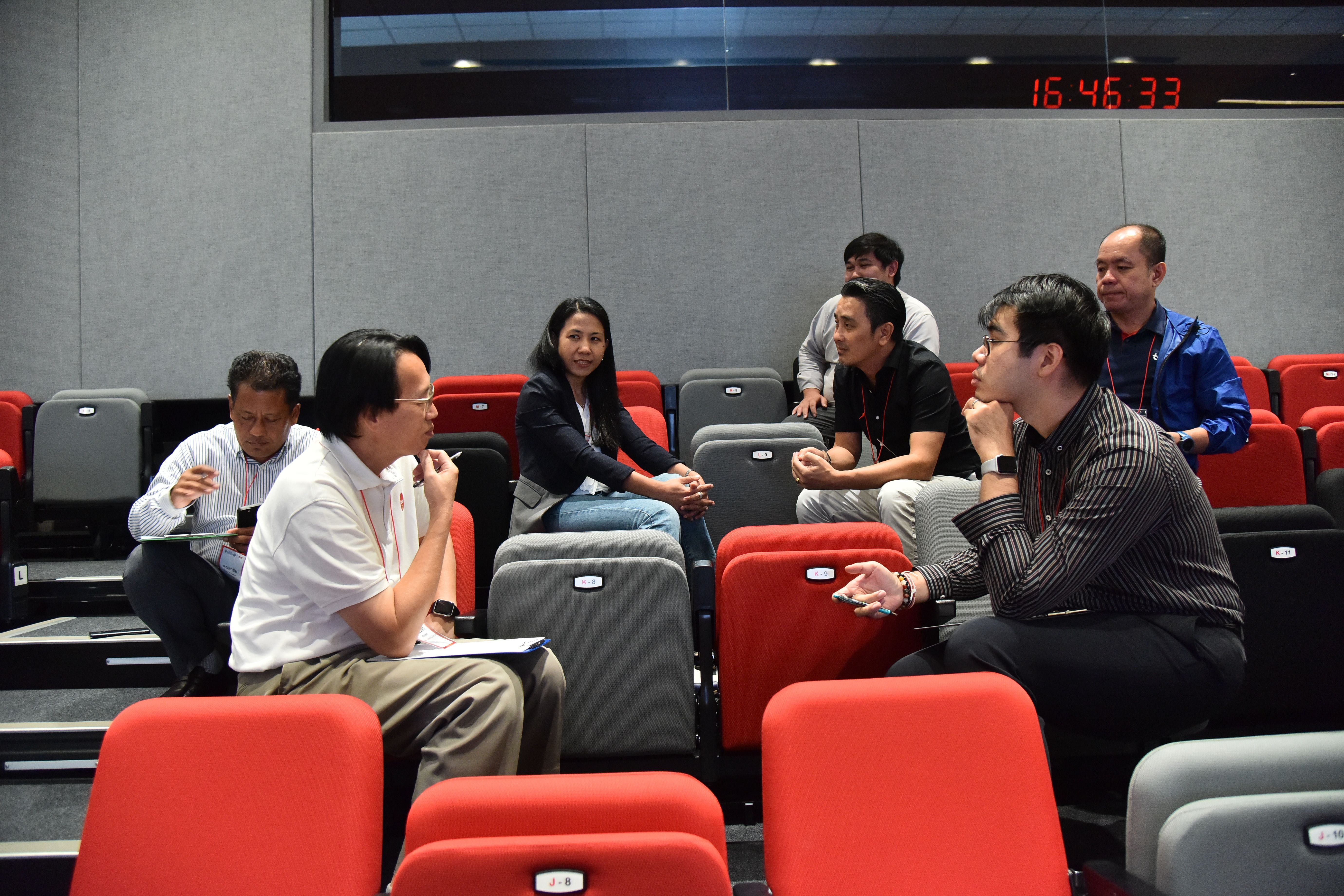 A group of professionals sit on suitcases in a modern meeting room, engaged in discussion.