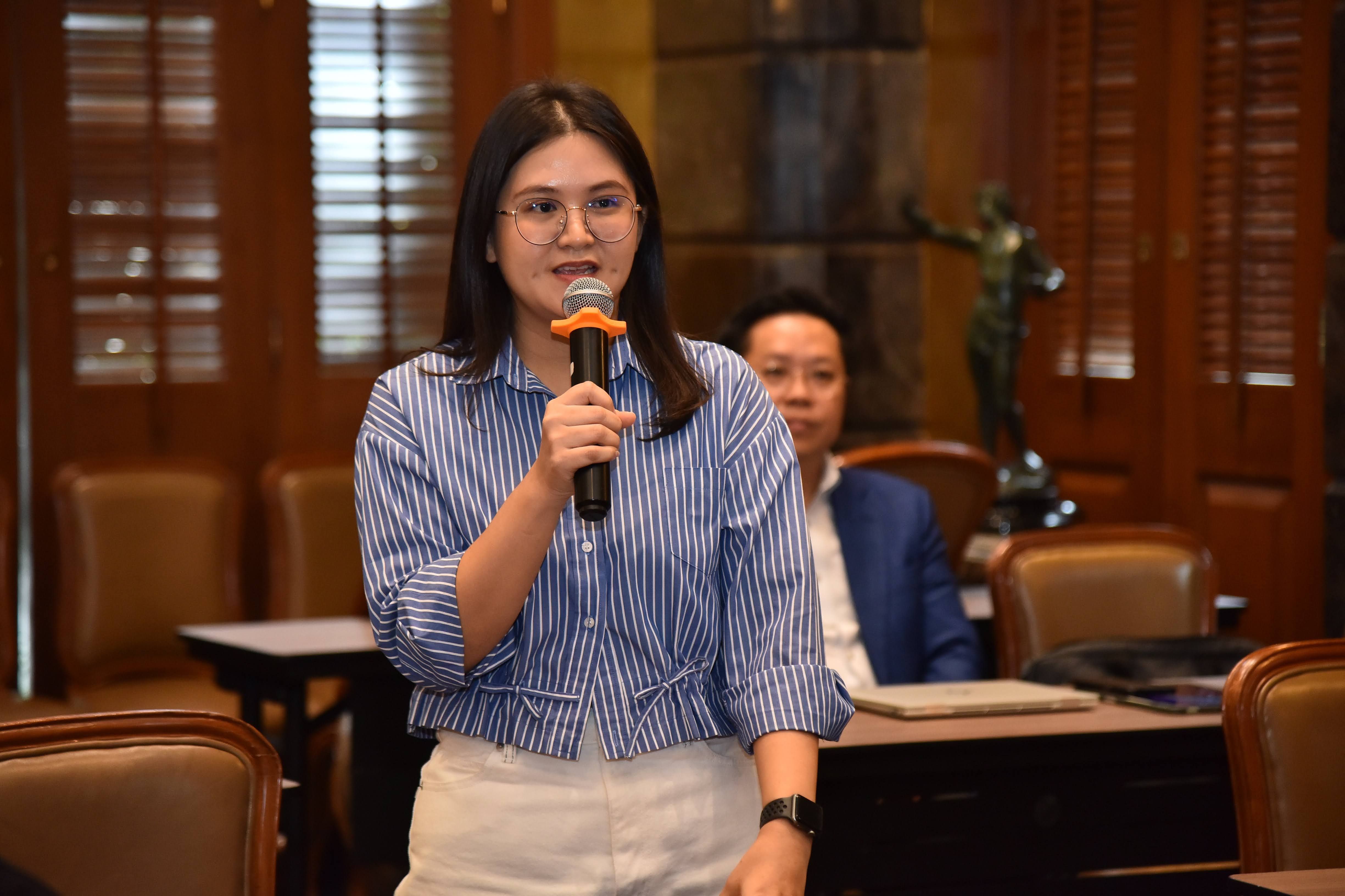 Woman with glasses speaking into a microphone during a presentation in a meeting room.