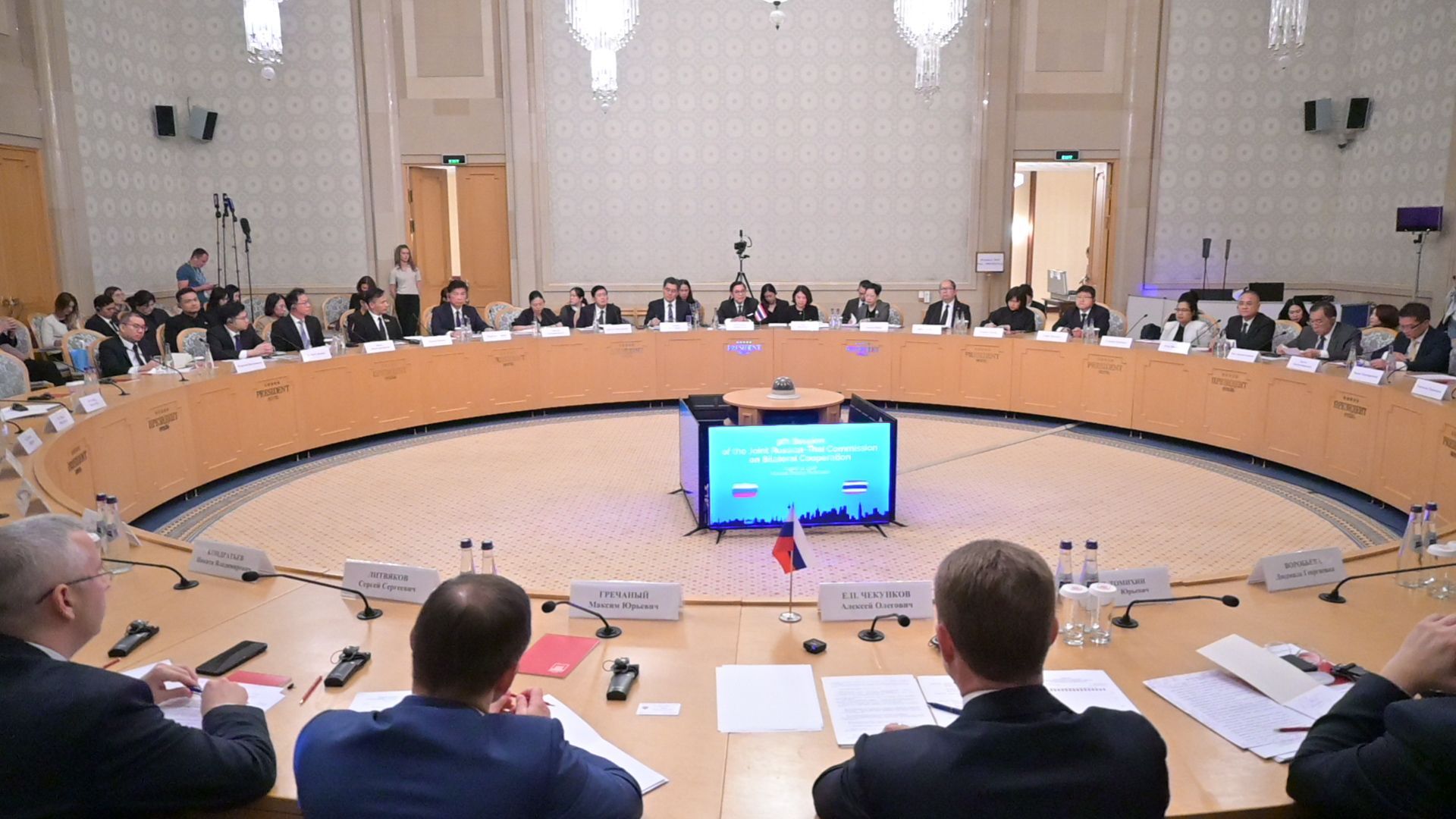 People seated around a large circular conference table with a central monitor showing a map.