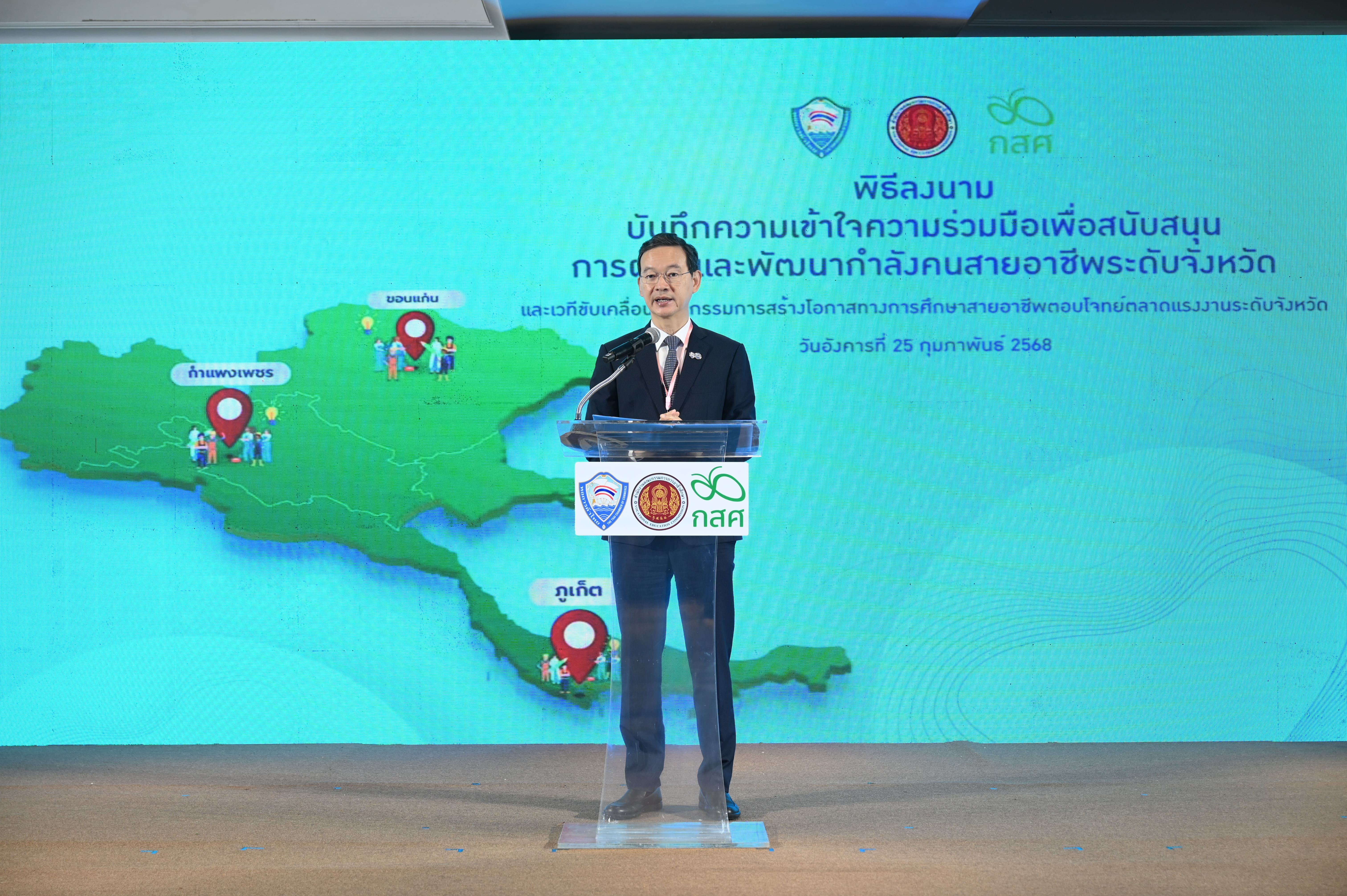Man speaks at podium before a screen displaying a map of Thailand and Thai text.