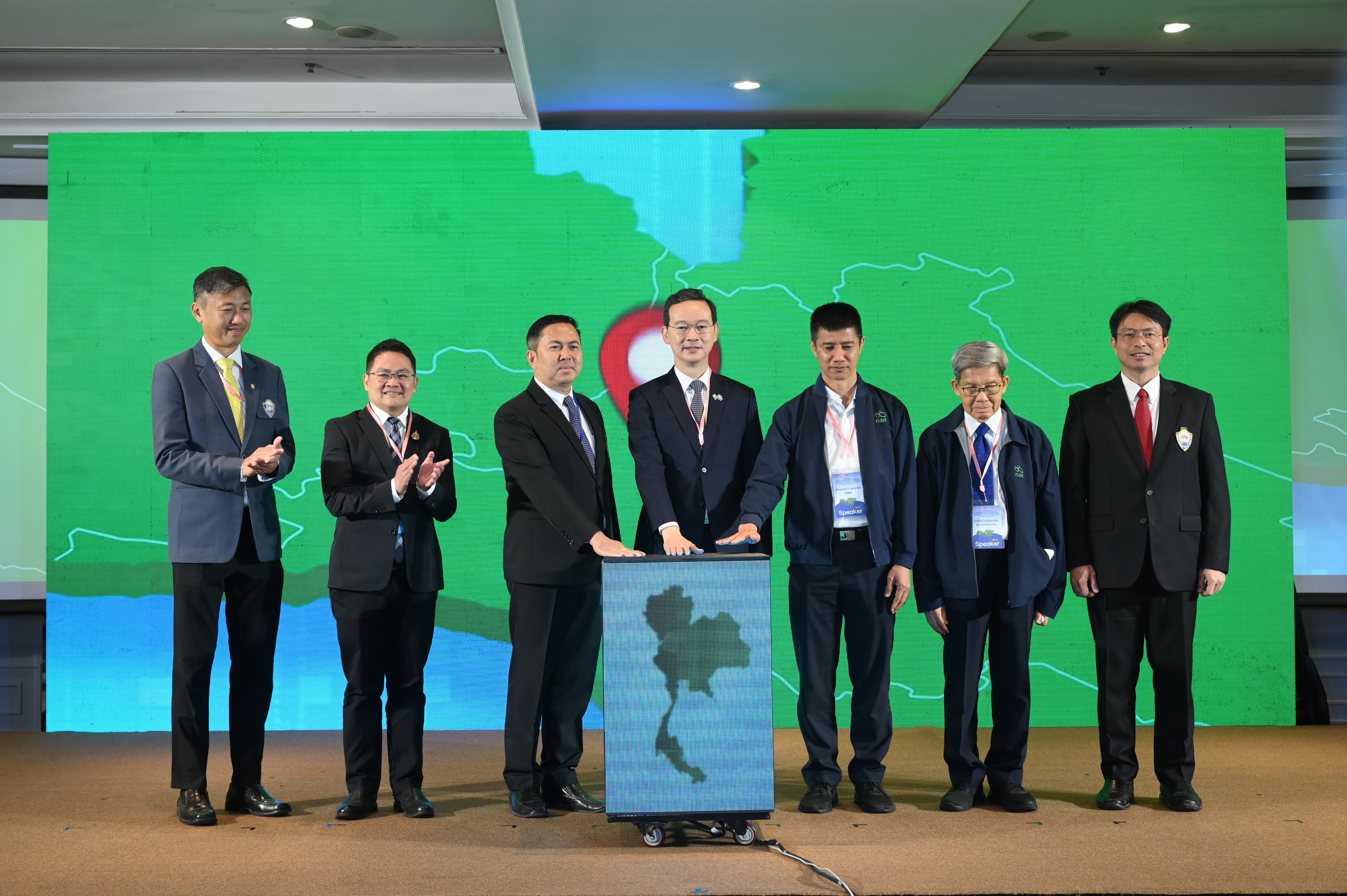 Seven men in suits launch an event with a glowing map before a green screen.