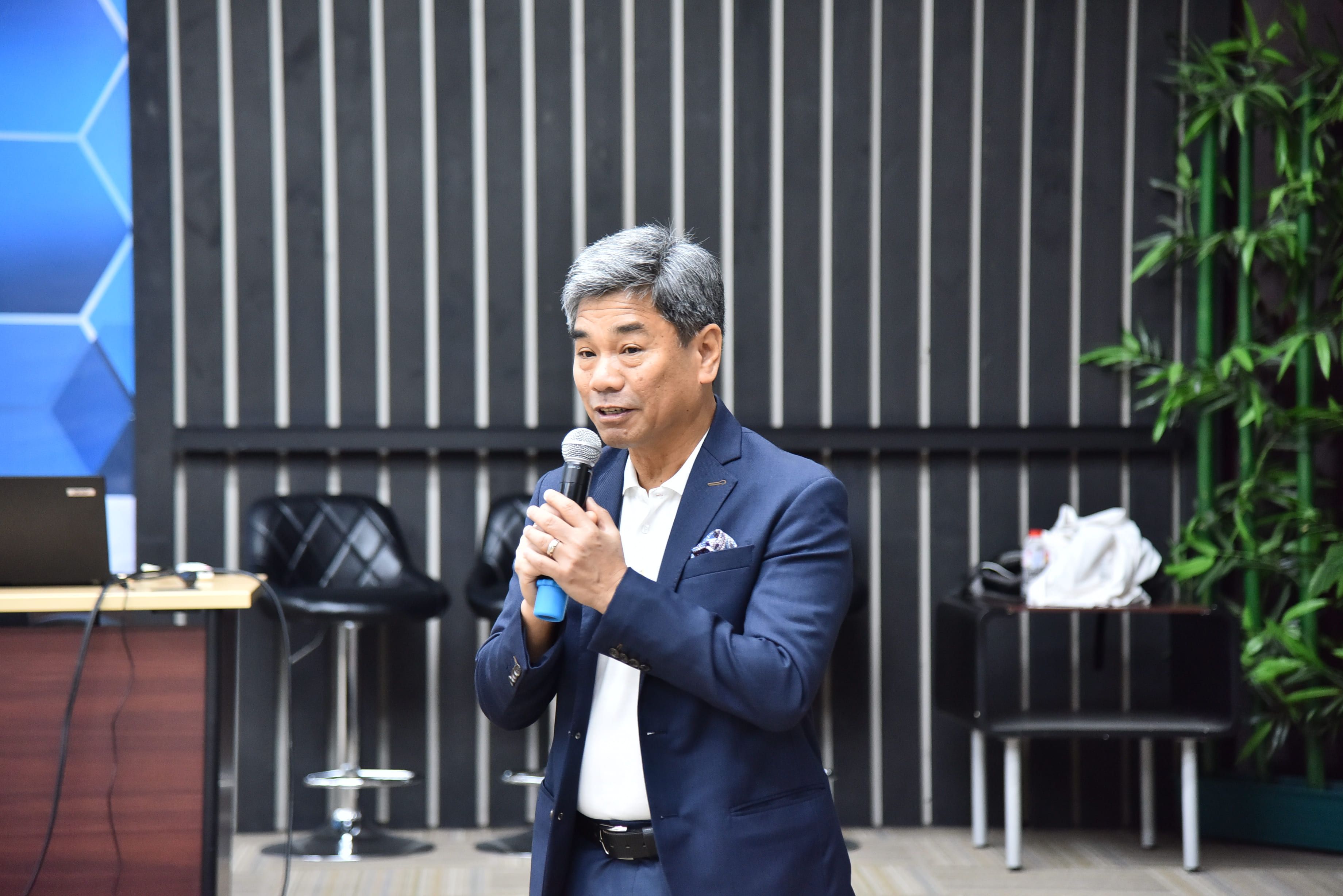 Man in blue suit speaking into a microphone at a presentation event.