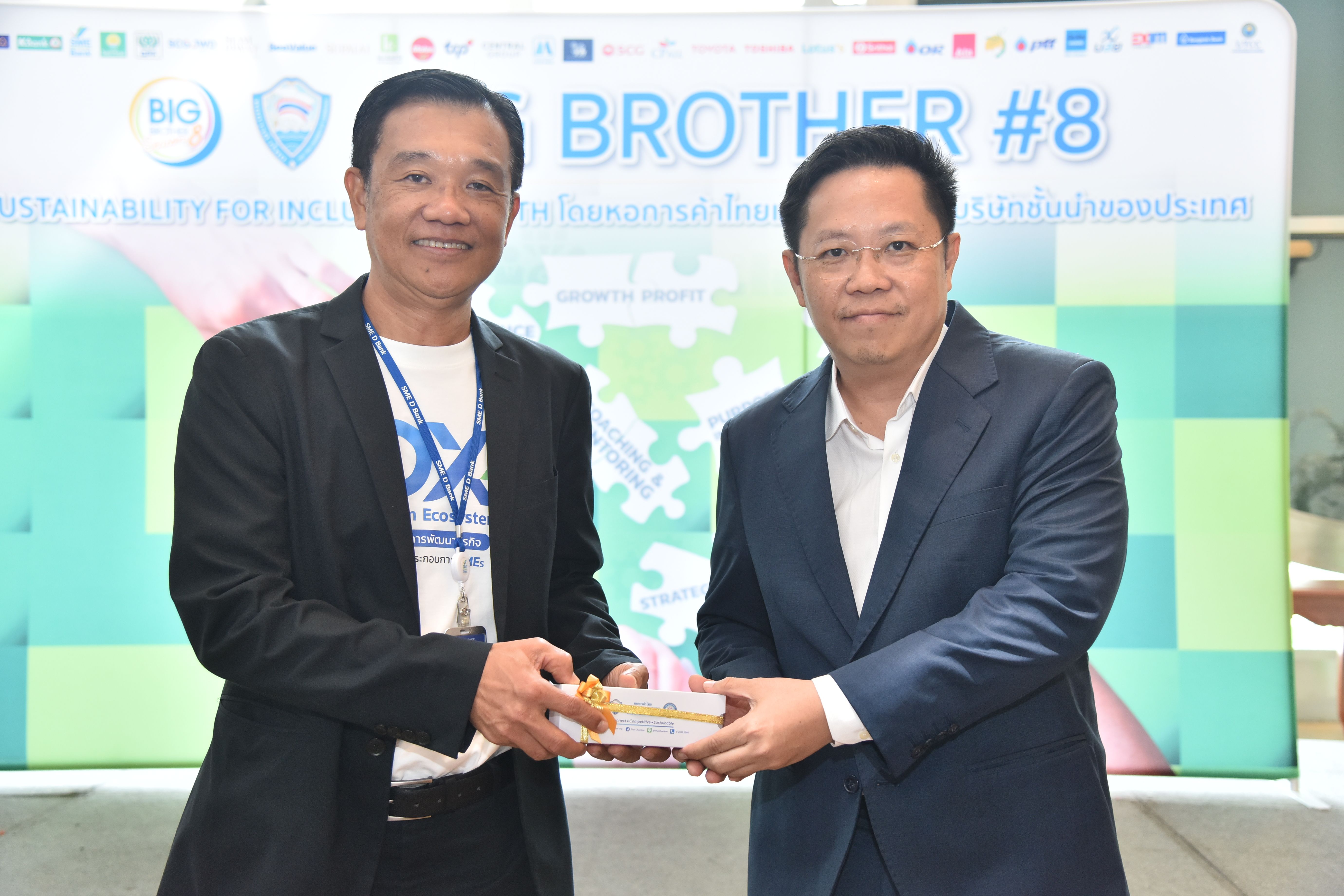 Two men smiling while exchanging a small gift or award at an event.